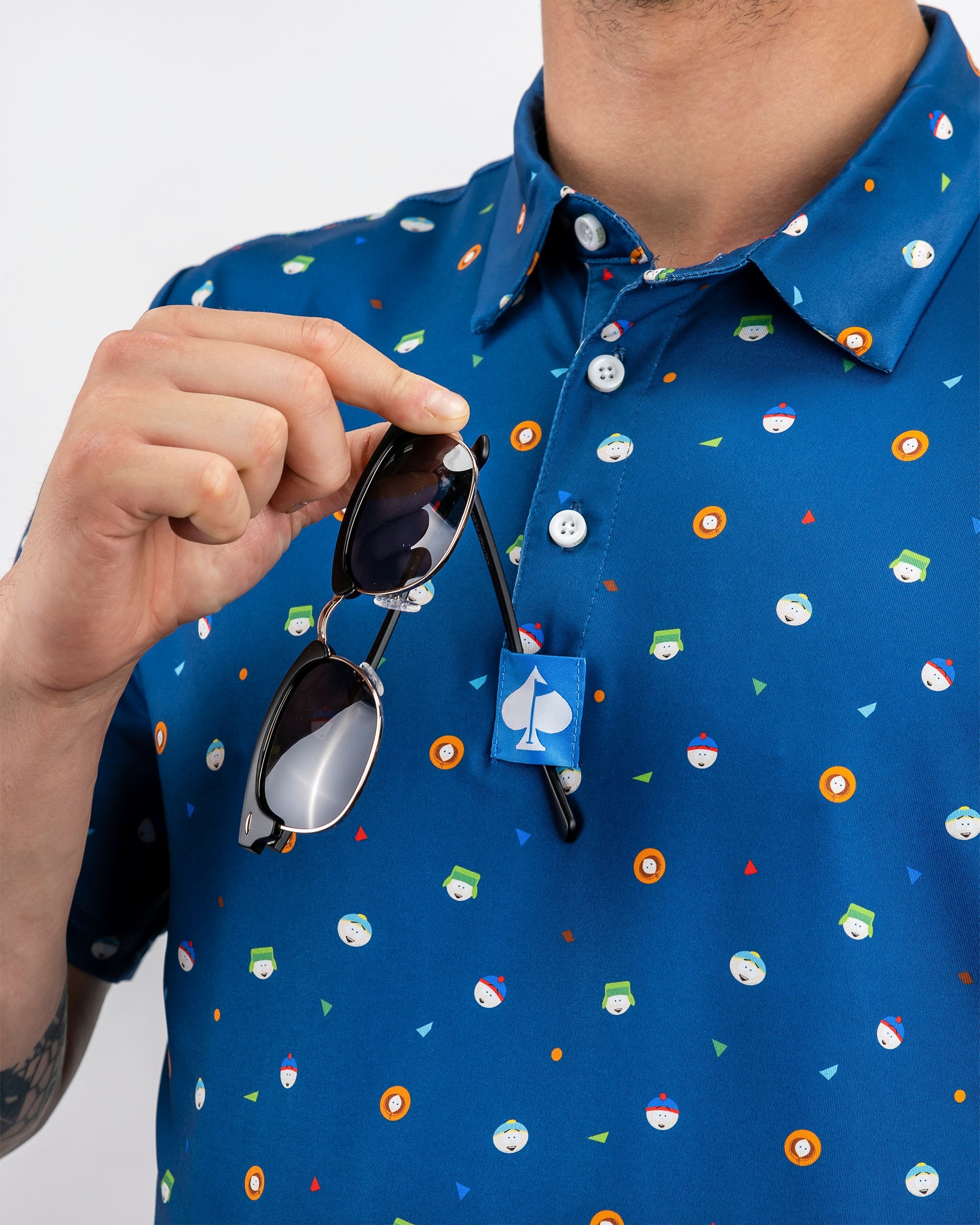 Blue polo shirt featuring a playful South Park design with colorful characters and icons, held by a person with sunglasses.