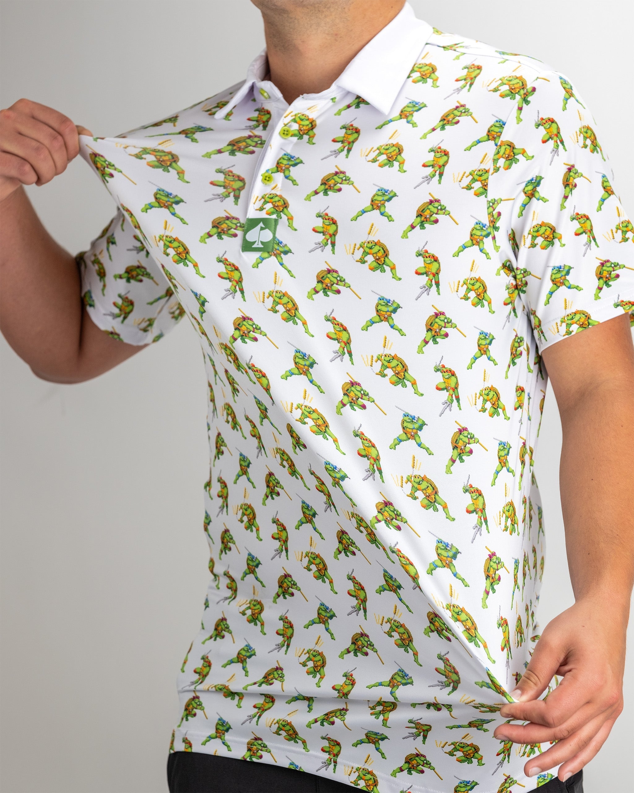 A golfer showcases a white polo shirt featuring a vibrant 8-bit design of Teenage Mutant Ninja Turtles in action.