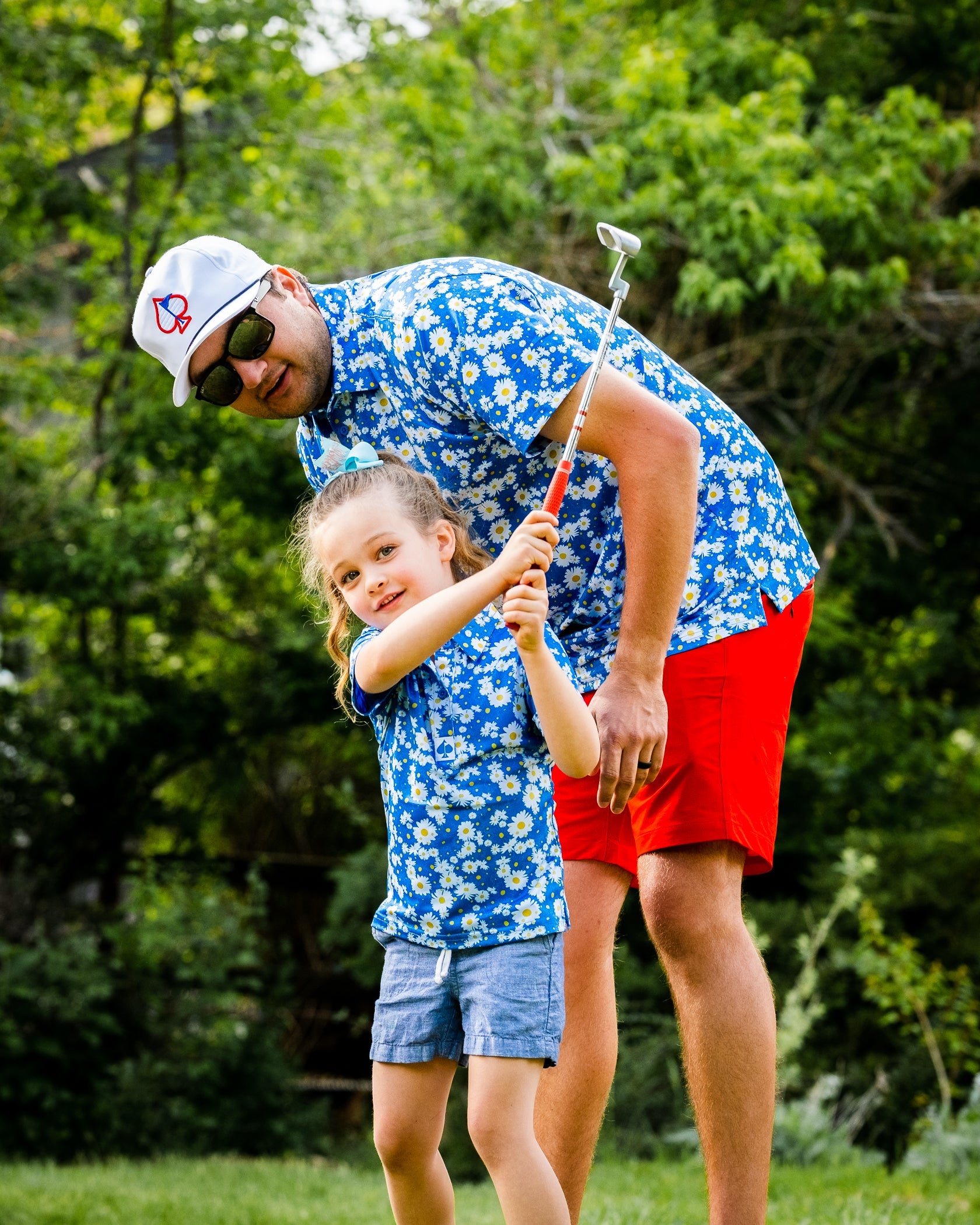 Youth girls' Daisies Polo worn by a girl golfing with an adult in a matching floral shirt, set in a green outdoor space.