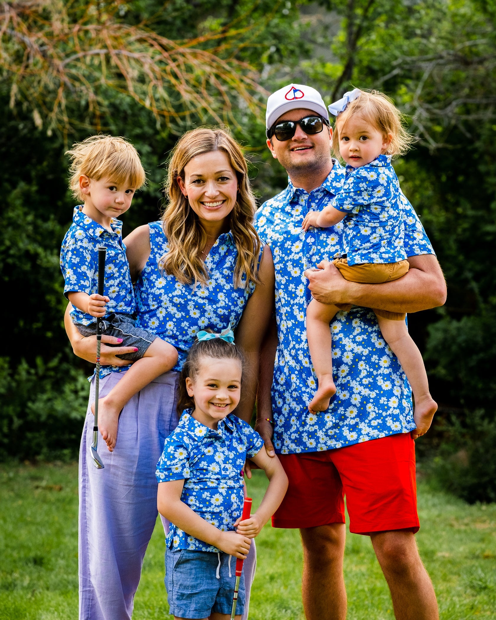 Family wearing matching blue floral polo shirts, enjoying a sunny day outdoors, showcasing the Youth Girls Daisies Polo.