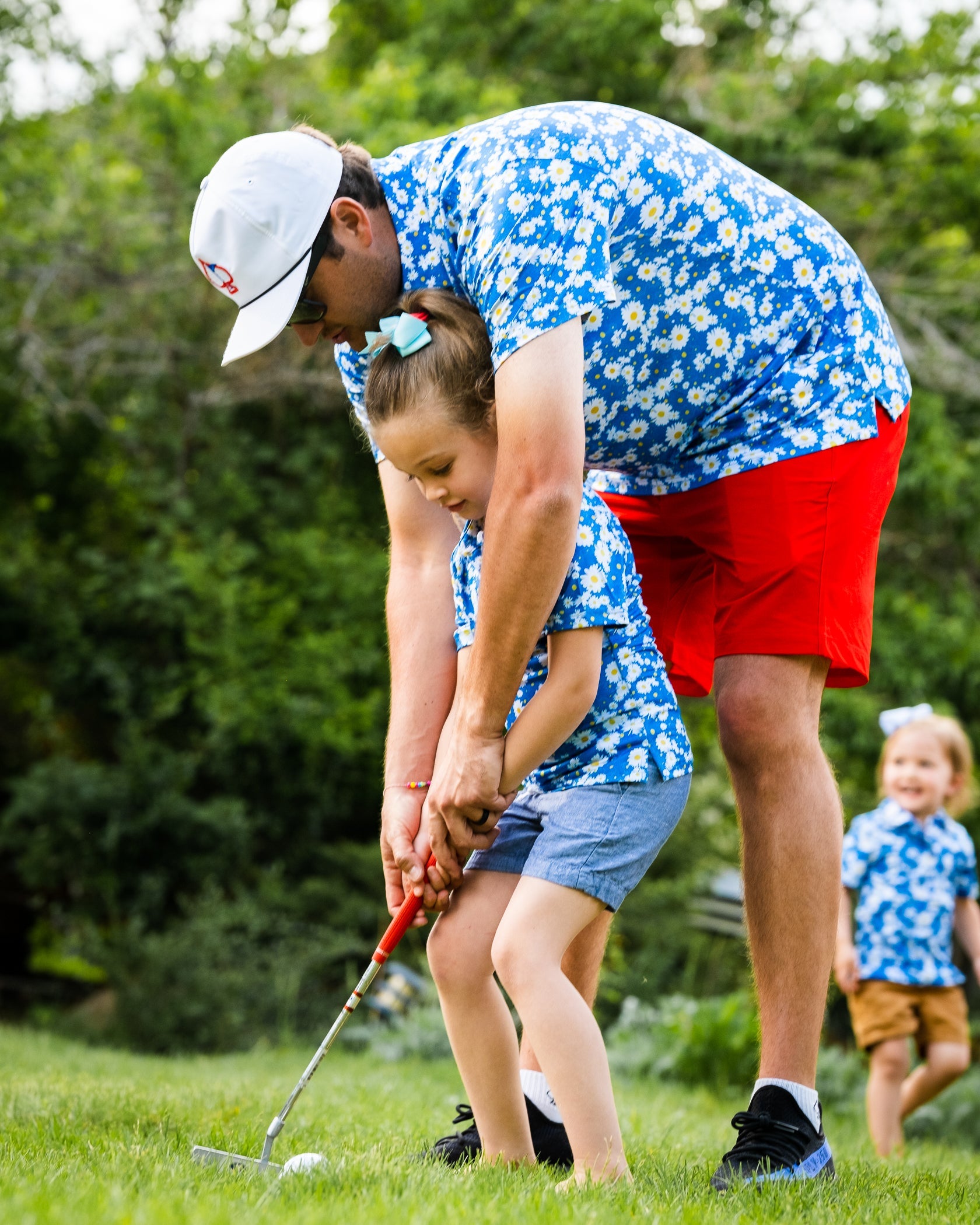 Youth girls' Daisies Polo worn by a girl and her father, both in matching floral shirts, practicing golf together outdoors.
