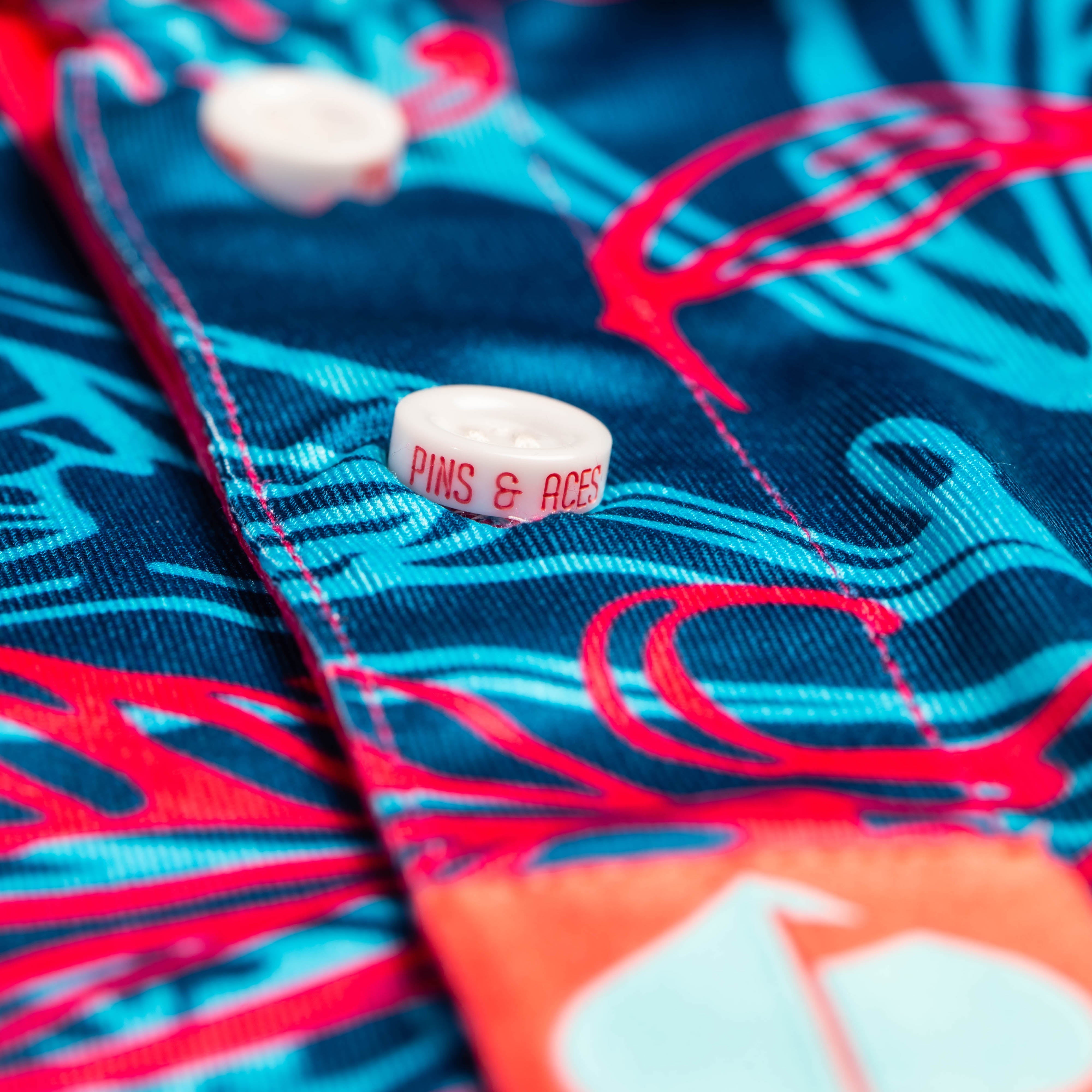 Bold Cabo Colada golf shirt featuring vibrant blue and pink tropical patterns with a branded button detail.