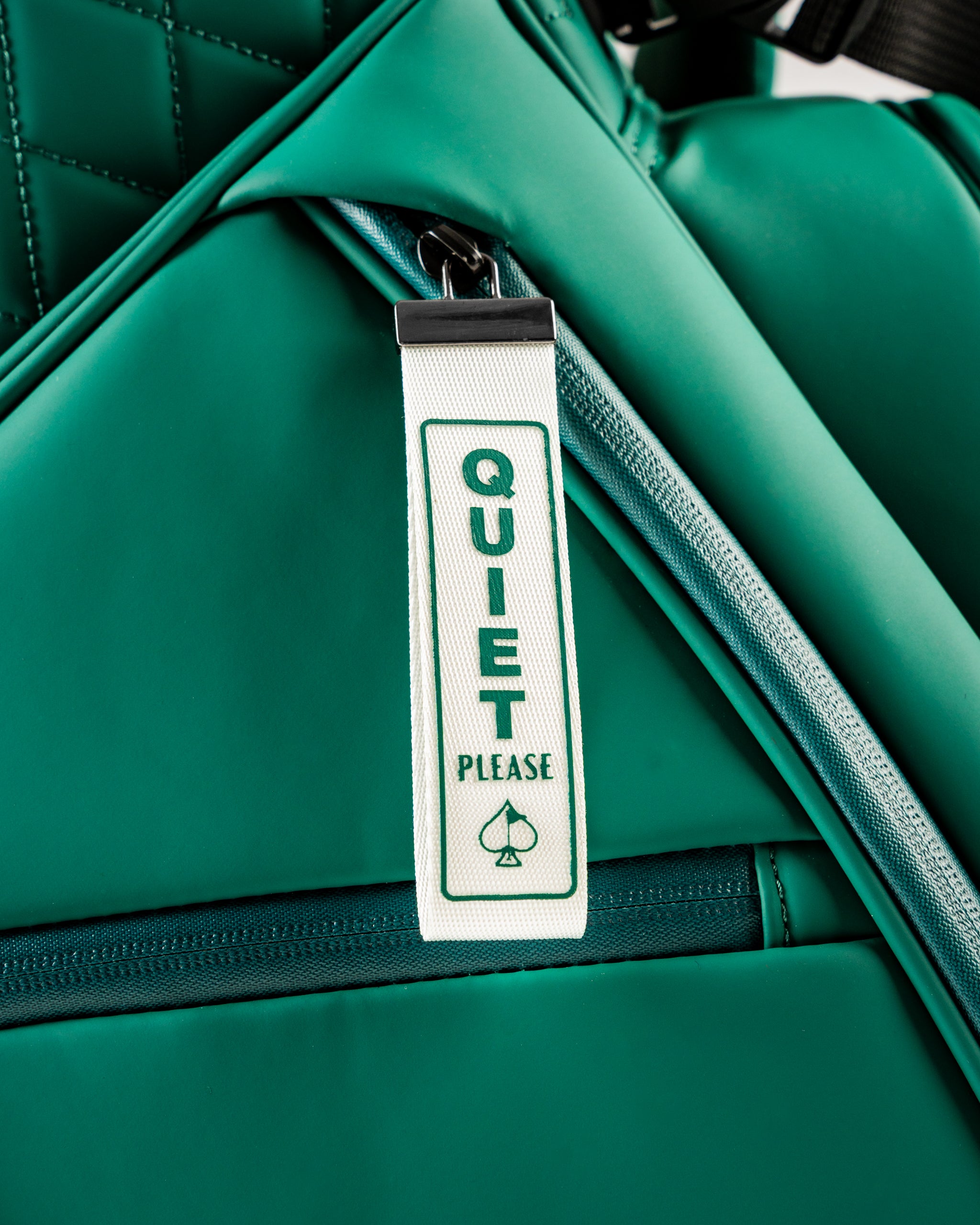 Close-up of a green golf bag featuring a tag that reads "Quiet Please," highlighting its stylish and functional design.
