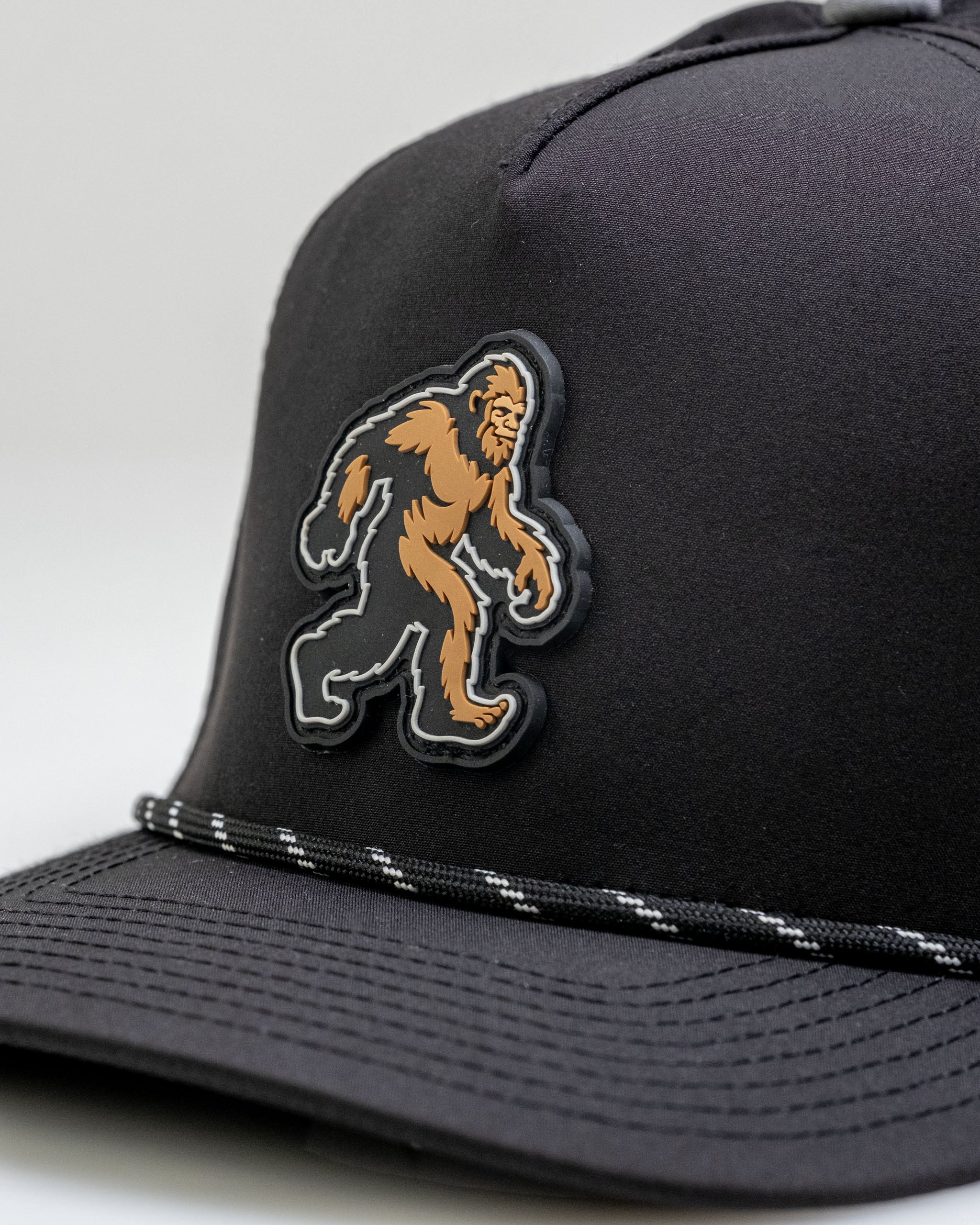 Black cap featuring a bold Sasquatch logo and a stylish striped band, perfect for golfers seeking unique apparel.