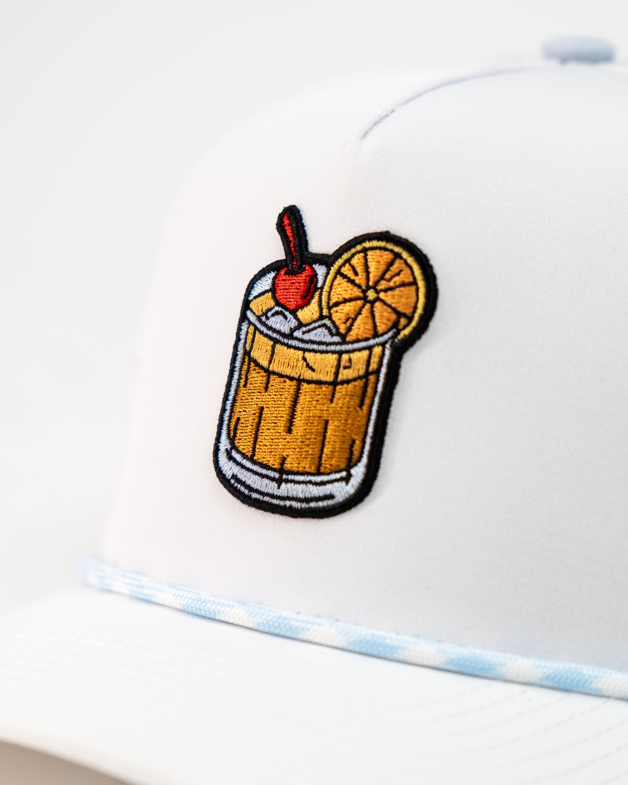 White perforated rope hat featuring an embroidered Old Fashioned cocktail design with a cherry and orange slice.
