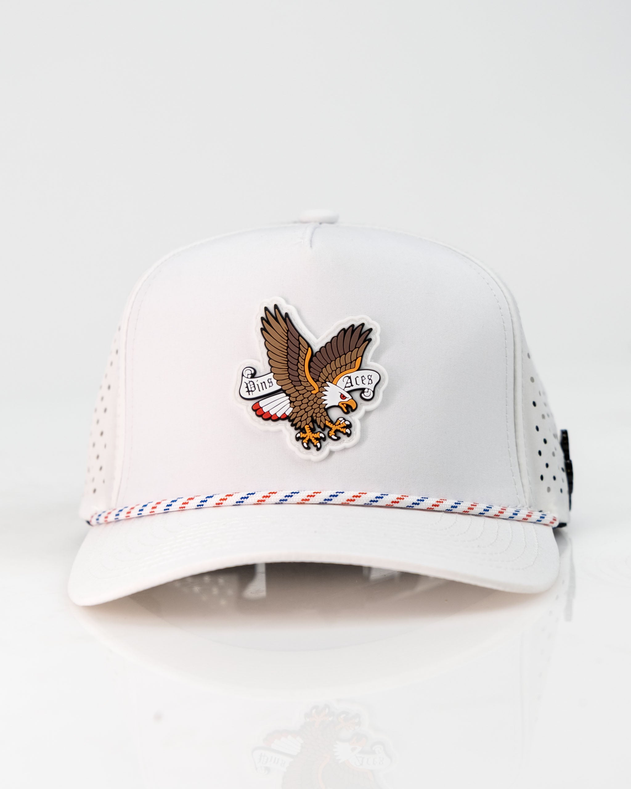 White perforated rope hat featuring an eagle design and "Pins and Aces" logo, perfect for stylish golfers.