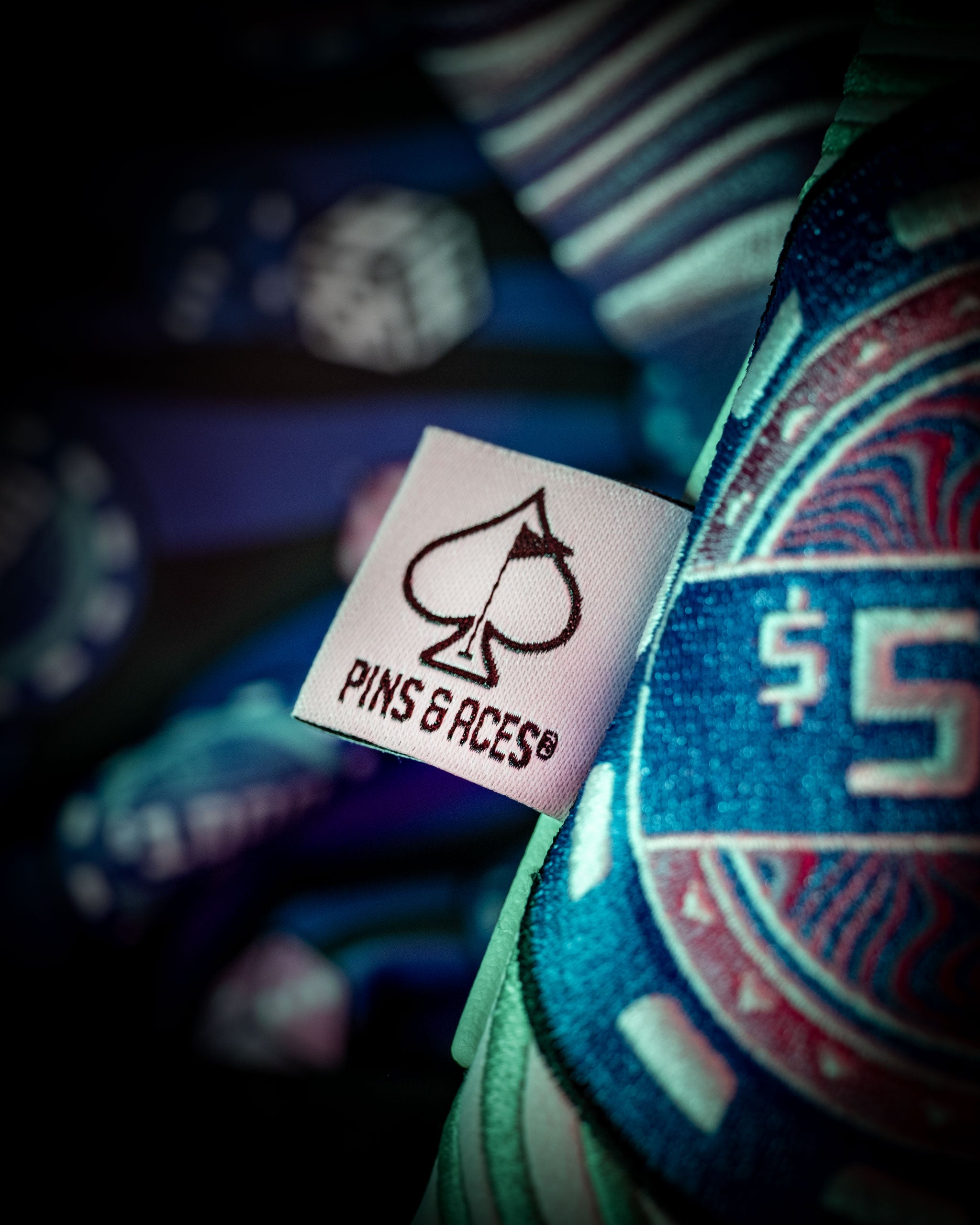 Close-up of the Pins and Aces logo on a colorful fabric, showcasing the unique design of the Mystery Box Backpack.