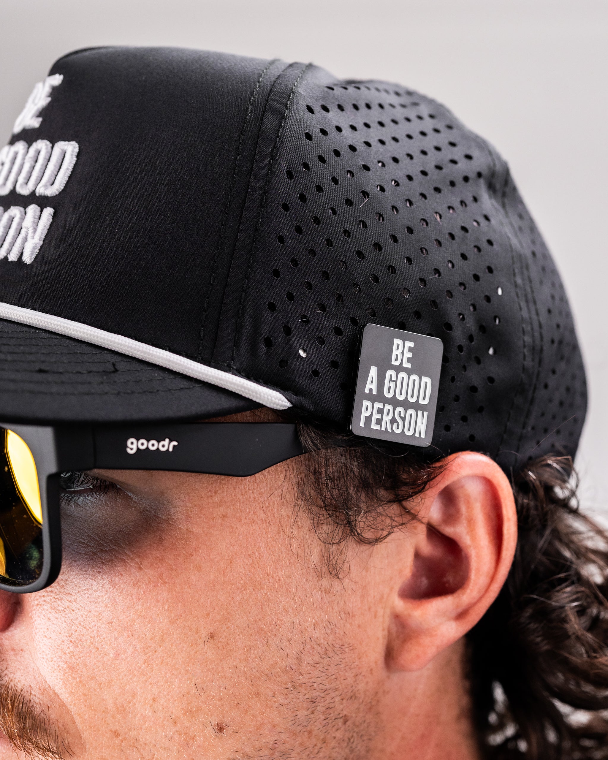 Black perforated rope hat featuring "Be A Good Person" text and a side tag, paired with stylish sunglasses.