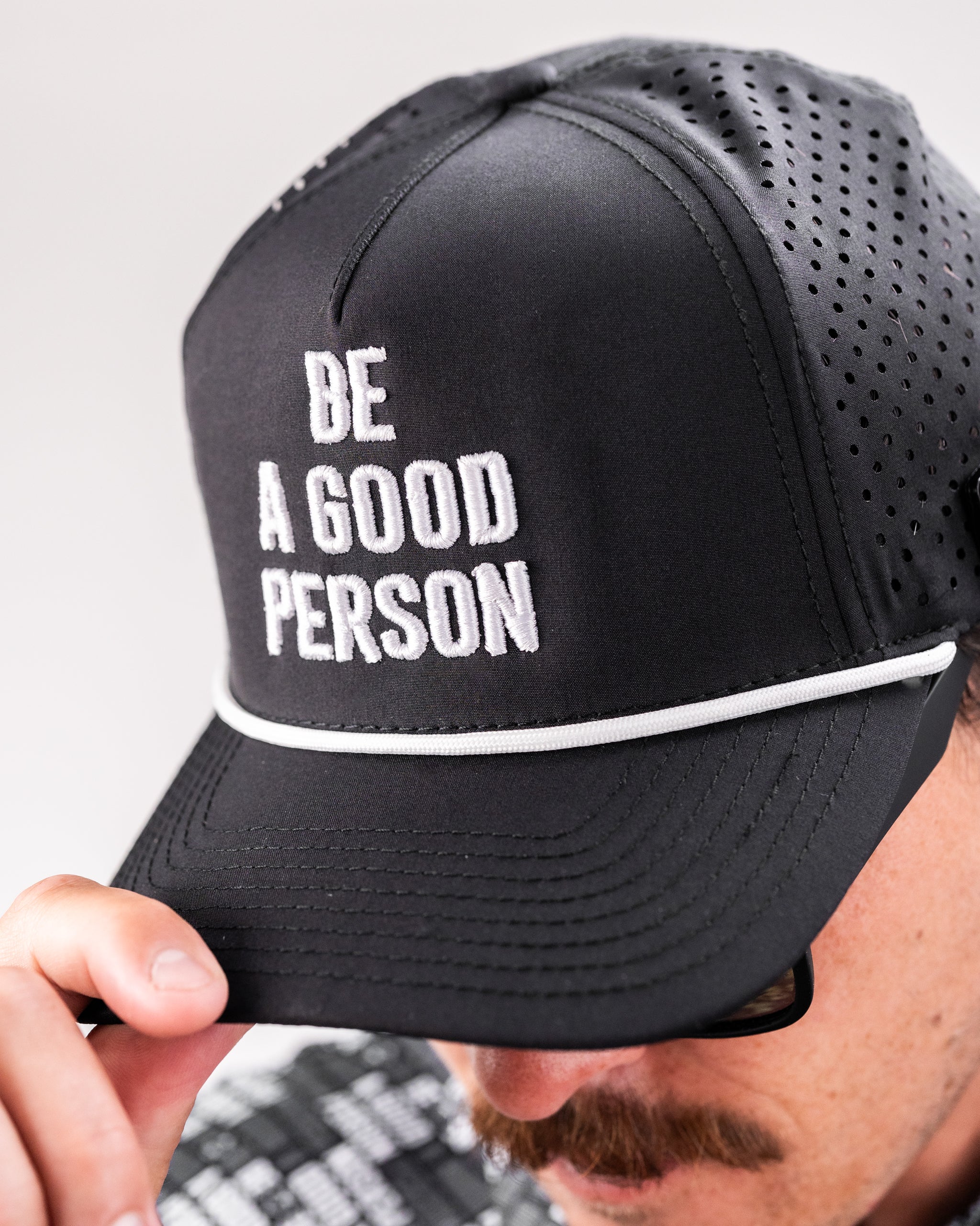 Black perforated rope hat featuring the phrase "Be A Good Person" in bold white letters on the front.