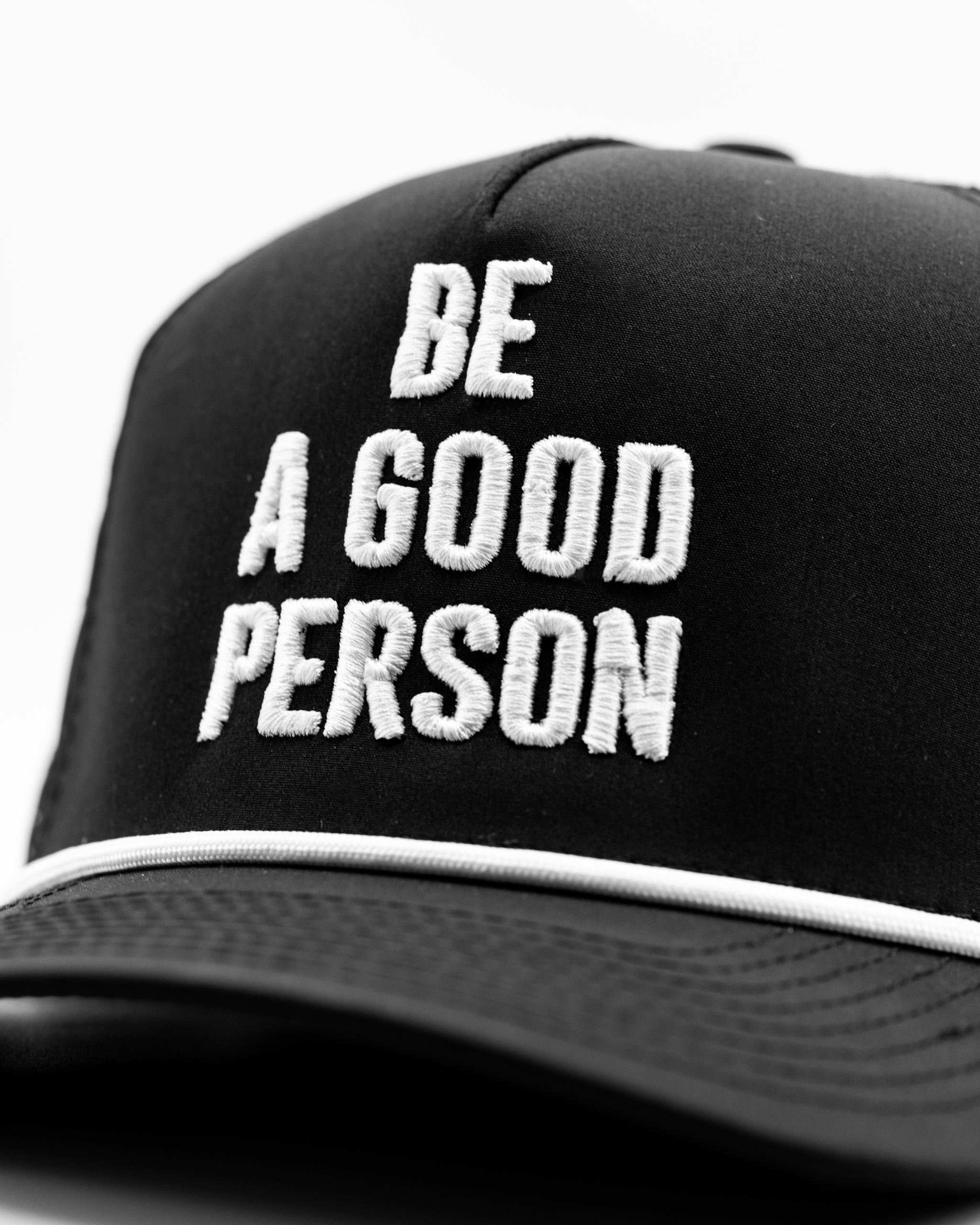 Black perforated rope hat featuring white embroidered text that reads "BE A GOOD PERSON." Stylish and bold design for golfers.