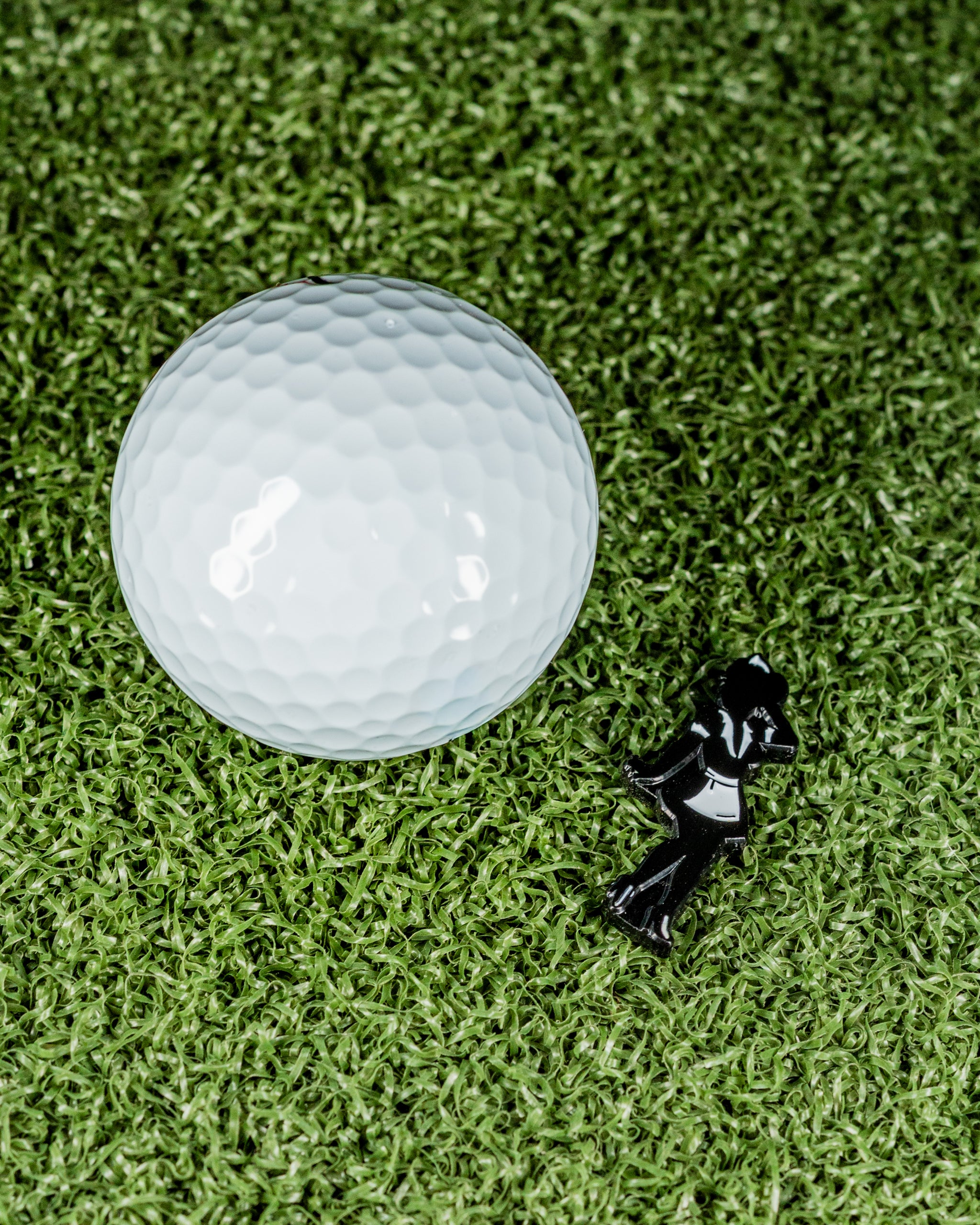 Black silhouette ball marker next to a white golf ball on green turf, ideal for stylish golfers.