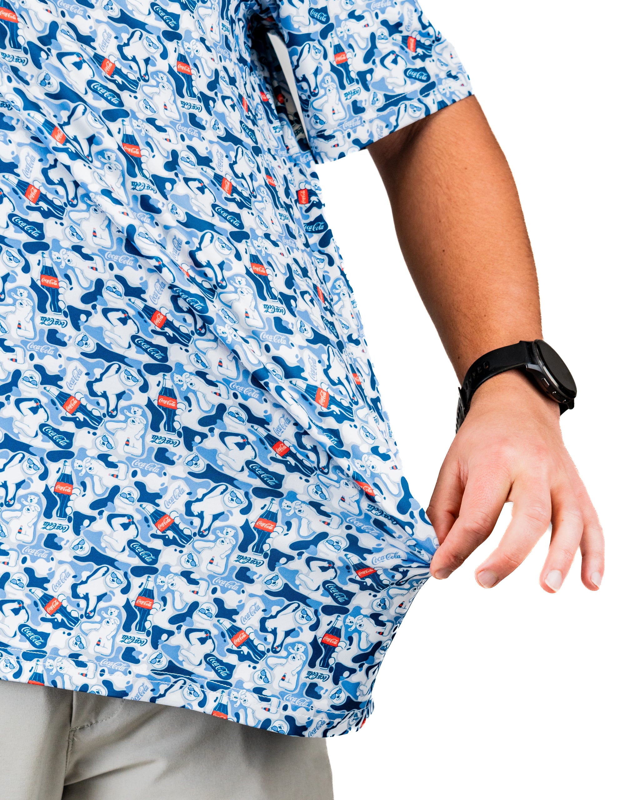 A person holds the hem of a short-sleeve shirt featuring a playful Coca-Cola pattern with blue and white colors.
