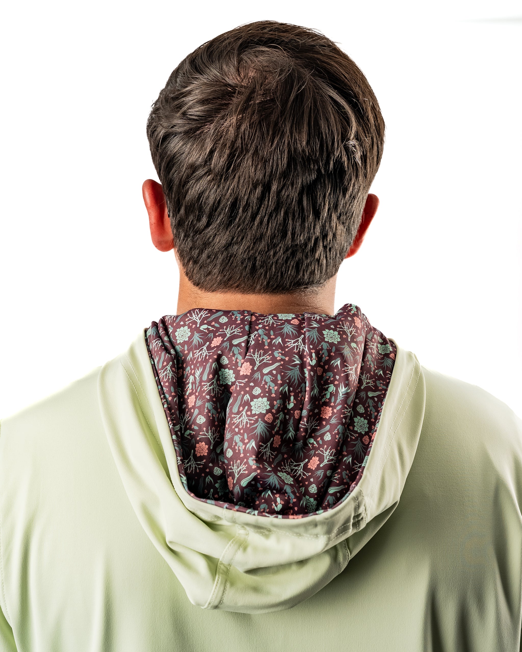 Back view of a man wearing a Desert Sage performance golf hoodie, featuring a floral-patterned interior lining.