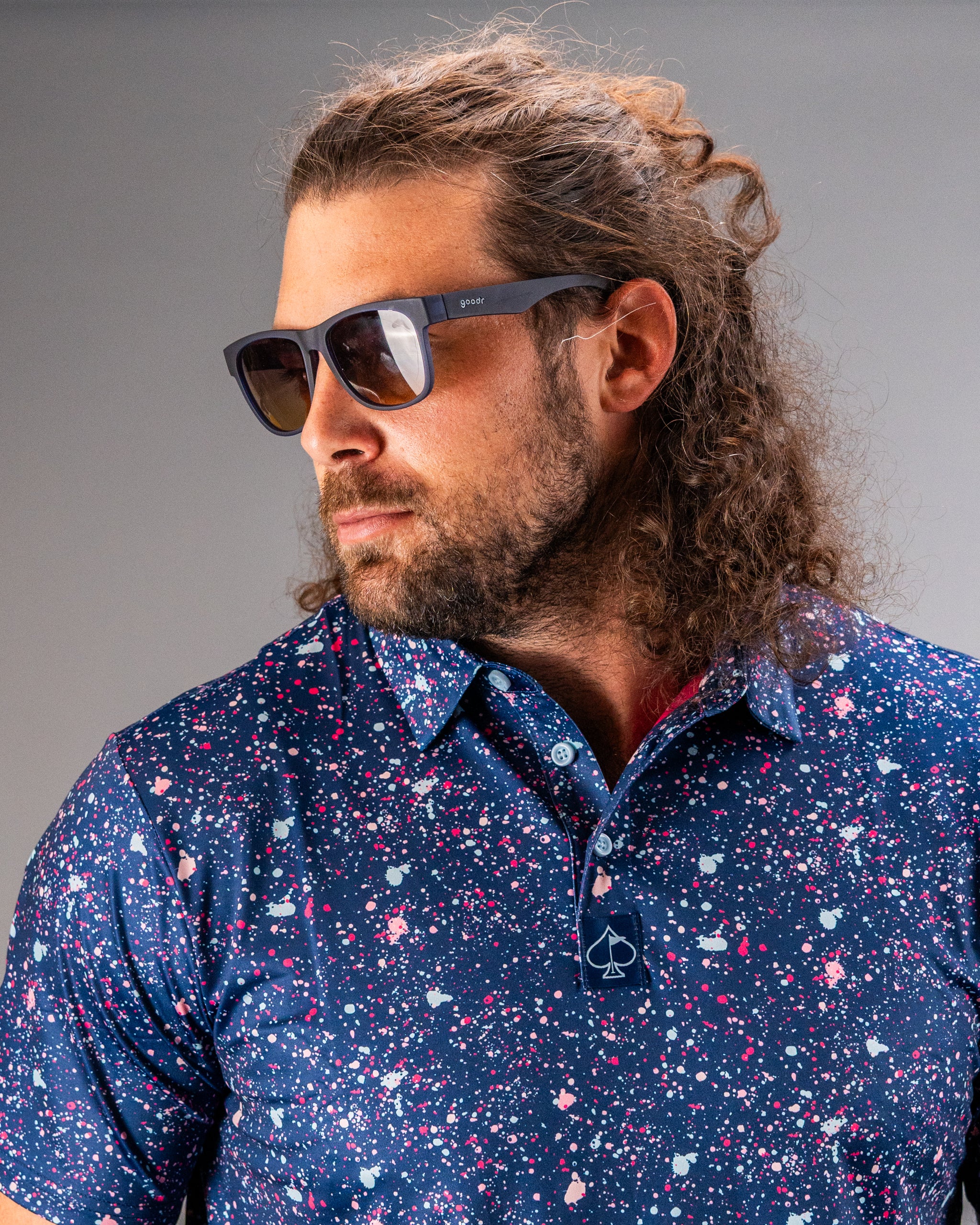 Man wearing a blue splatter golf shirt with a modern design, complemented by stylish sunglasses.