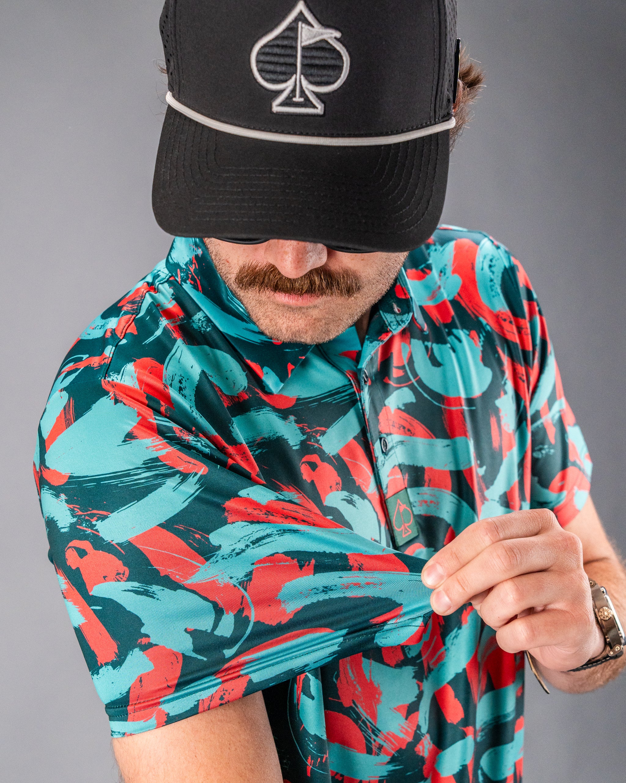 Bold golf polo shirt in Paint Strokes Coral featuring a vibrant abstract pattern in teal and coral hues.