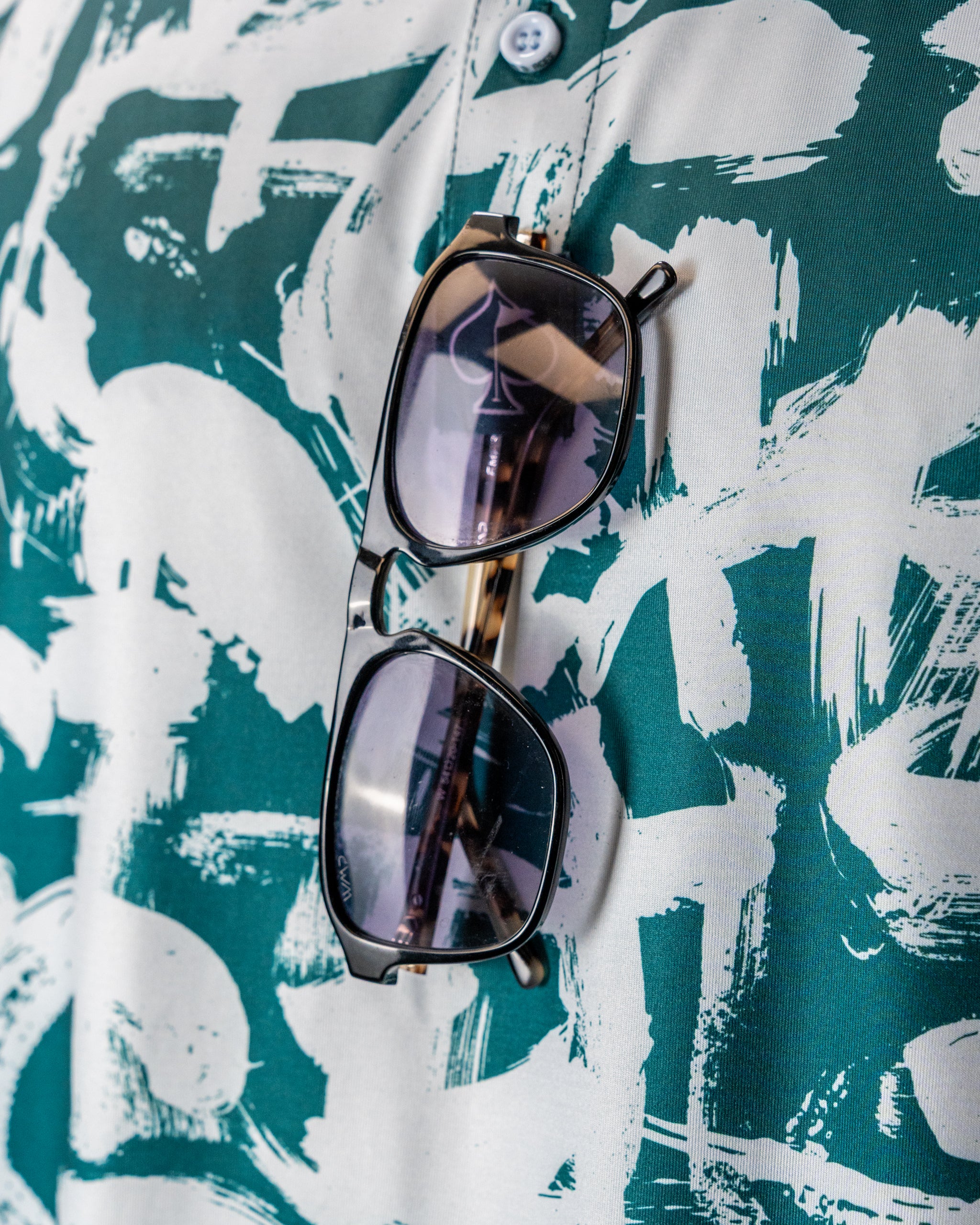 Bold green golf shirt featuring a paint stroke pattern, with stylish sunglasses resting on the fabric.