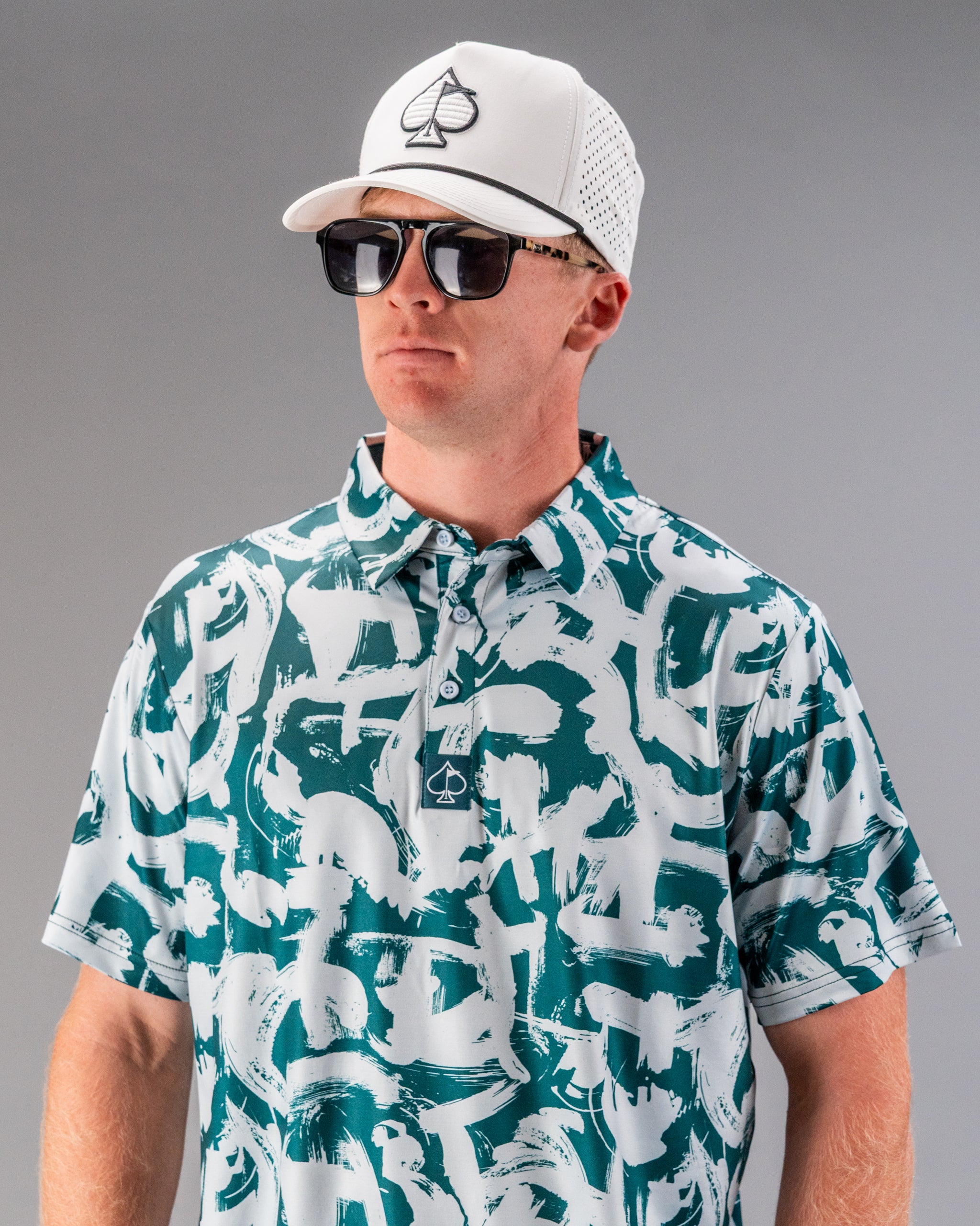 Bold green golf polo featuring a unique paint stroke design, paired with a white cap and sunglasses for a stylish look.