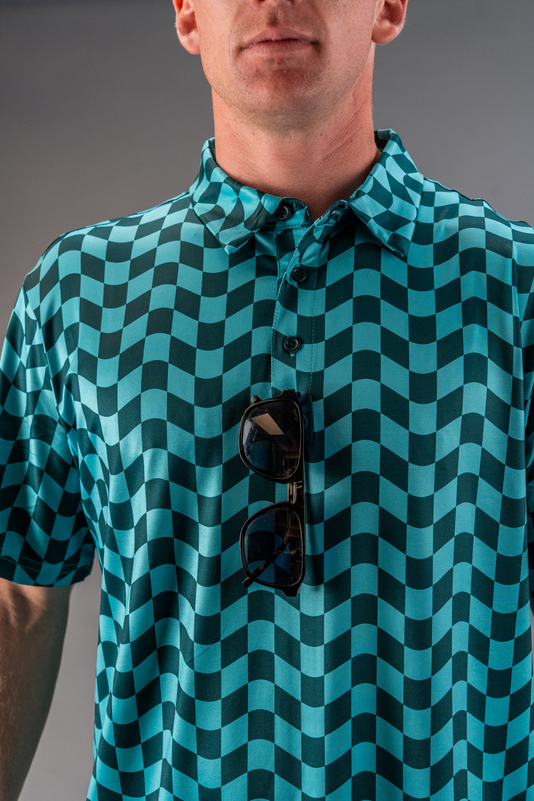 Bold wavy checkered golf polo in teal, featuring a button-up collar and sunglasses draped over the front.