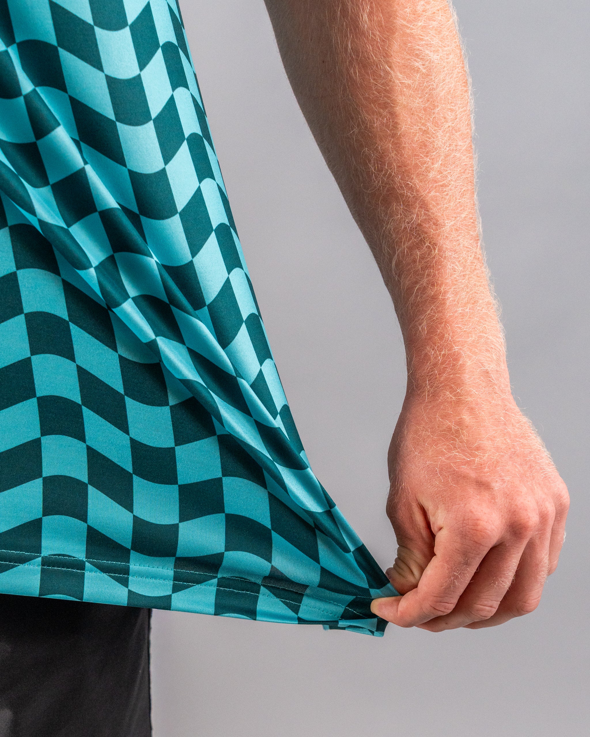 Close-up of a person holding the hem of a teal and black wavy checkered golf shirt, showcasing its unique pattern.