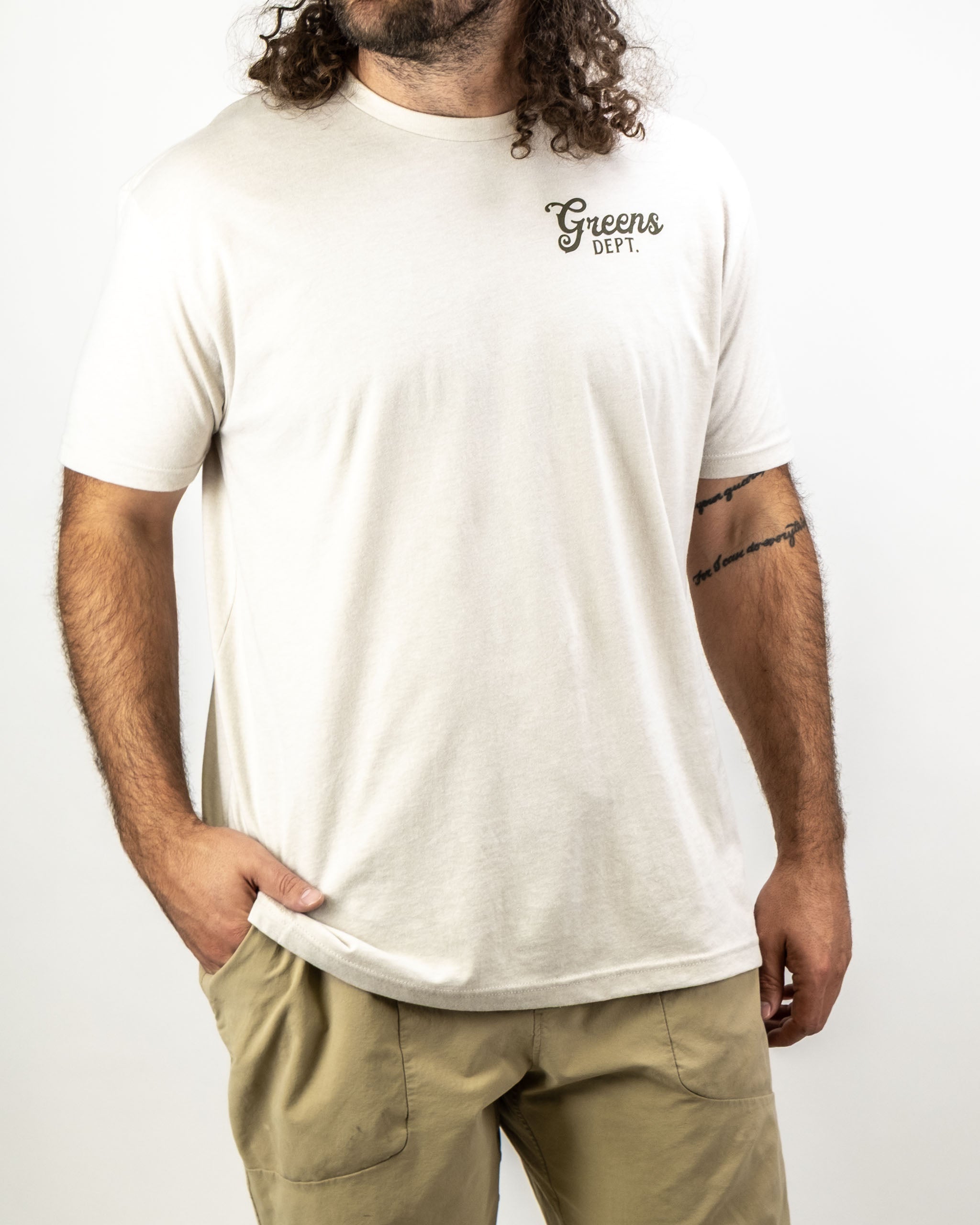 Men's cream-colored tee shirt featuring "Greens Dept." logo, perfect for stylish golfers on and off the course.