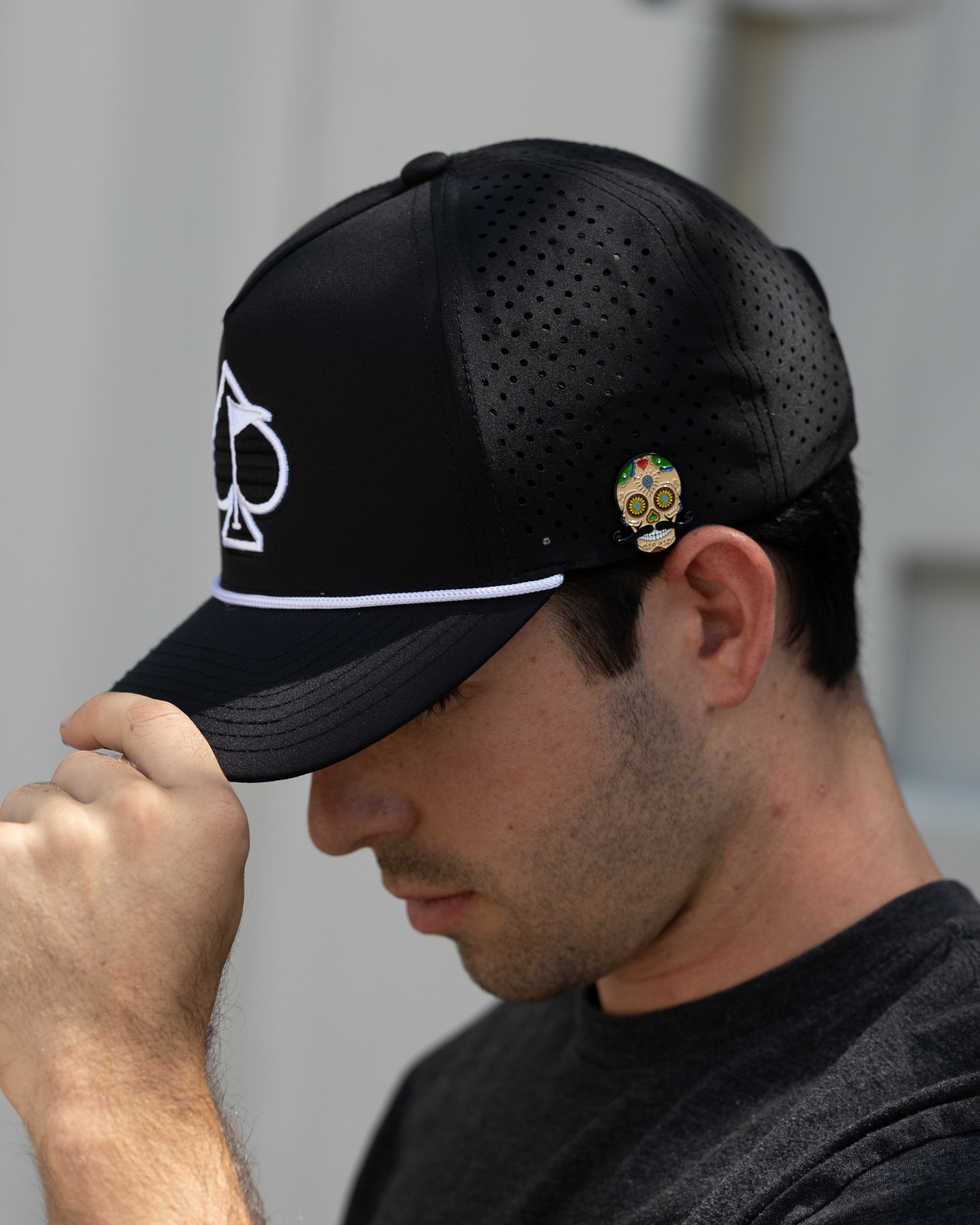Black golf cap with perforated panels, white piping, skull pin, and bold golf logo for standout style on the course.