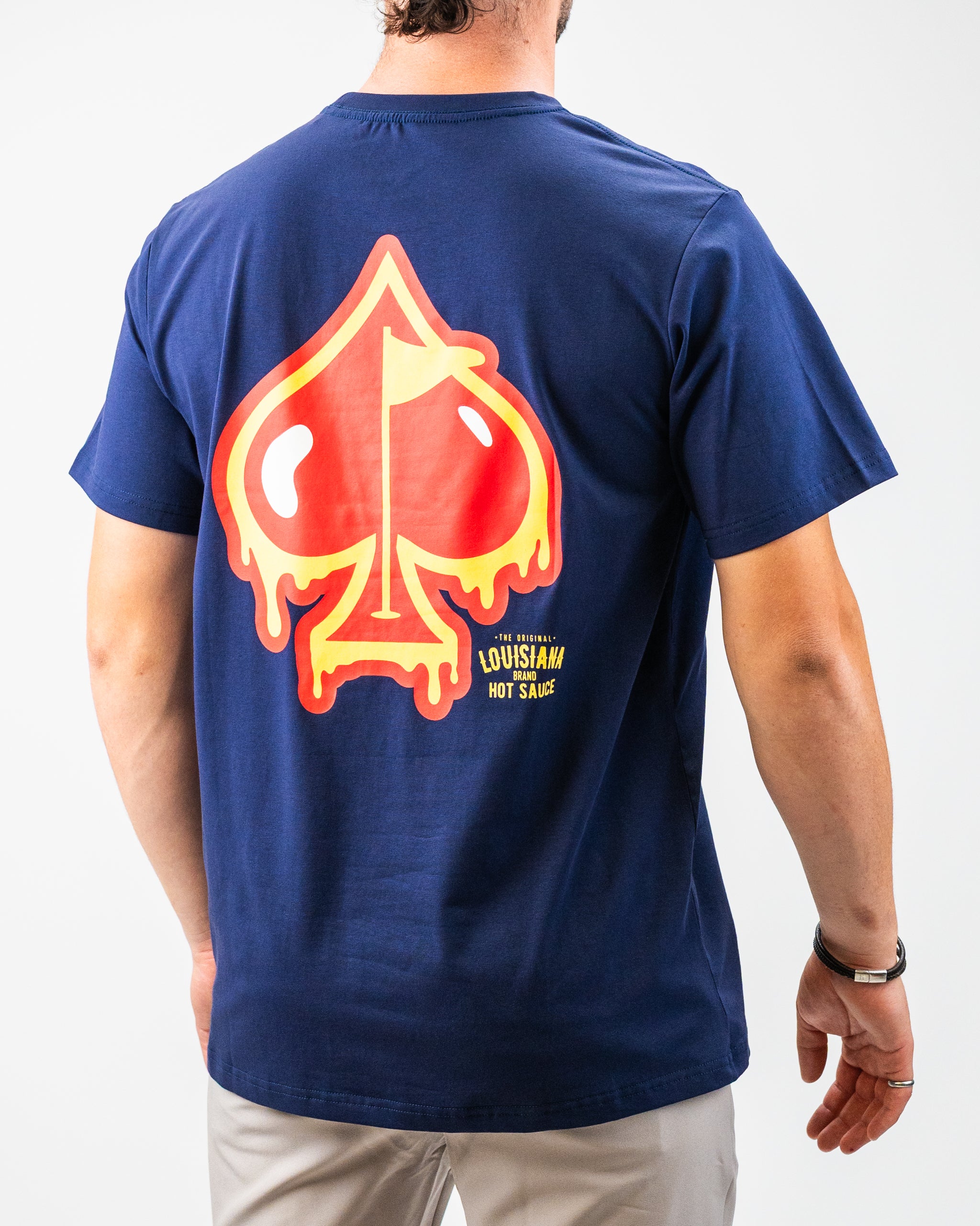 Back view of a navy blue golf t-shirt featuring a bold, melting hot sauce pepper graphic with "Louisiana Hot Sauce" text.