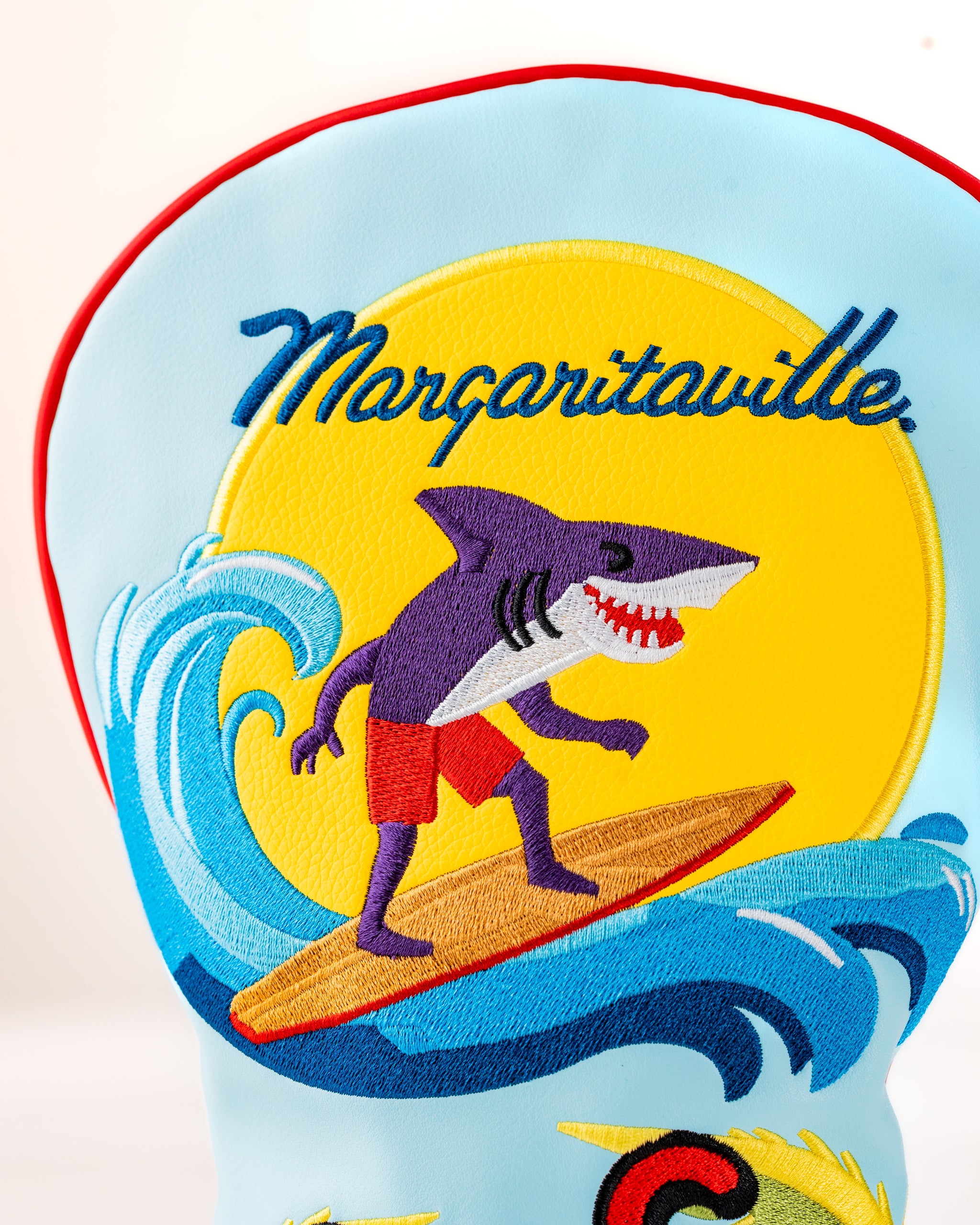 Margaritaville x Pins & Aces headcover set featuring a vibrant shark surfing design against a sunny backdrop.