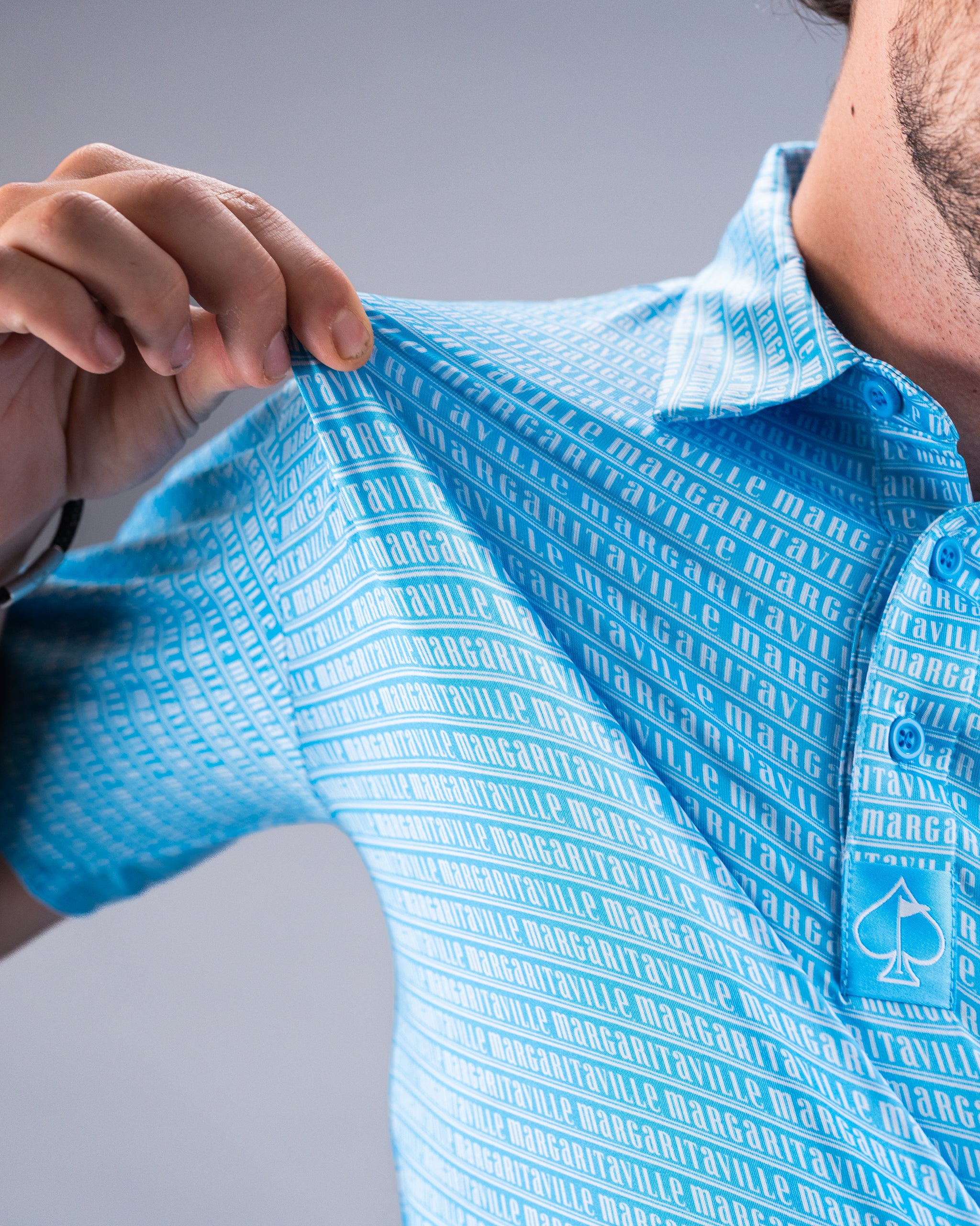 Close-up of a man adjusting a bright blue golf shirt with "MARGARITAVILLE" printed repeatedly in white, featuring a white ...