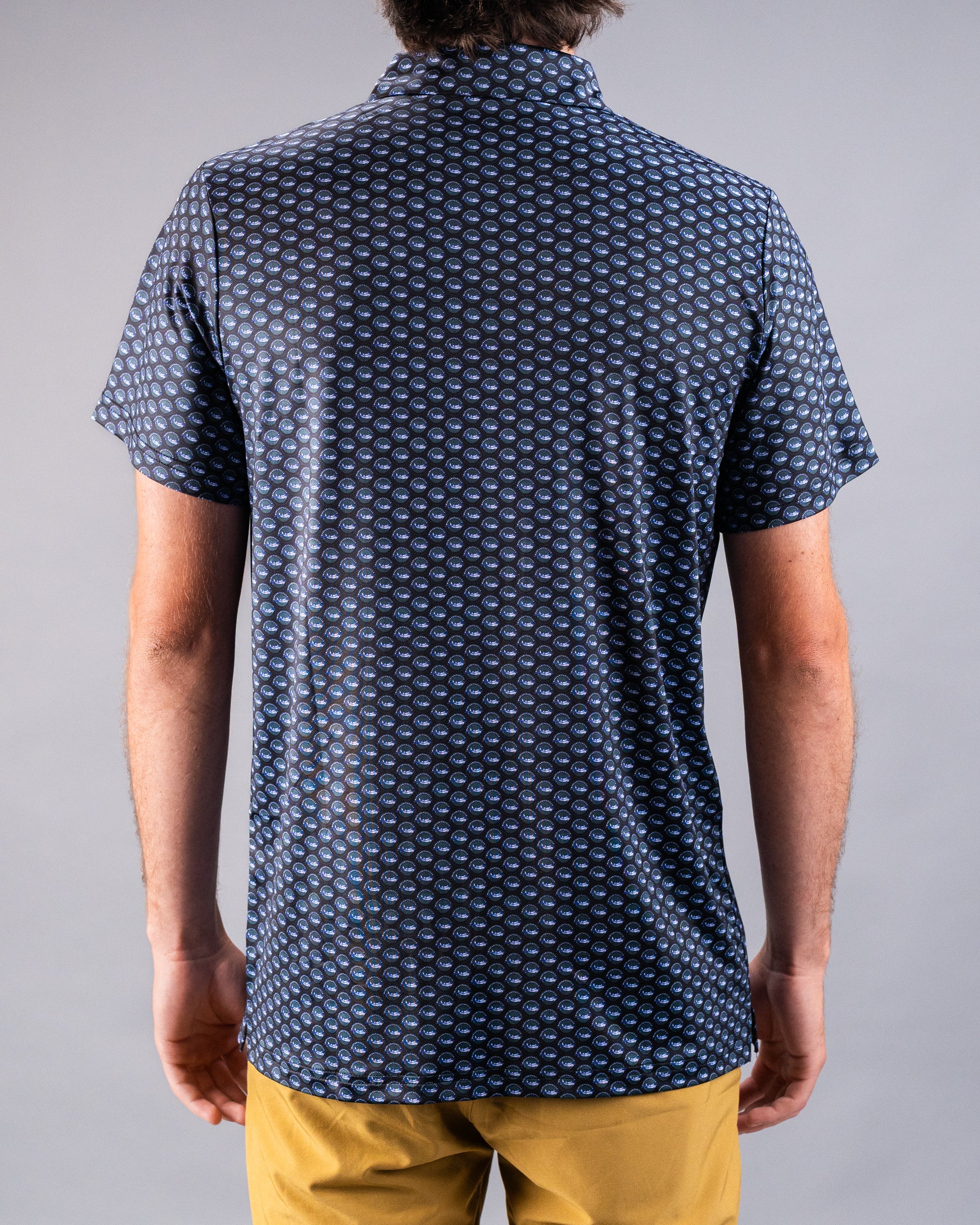 Back view of a navy blue golf shirt with a repeating blue and white circular pattern, paired with yellow pants.