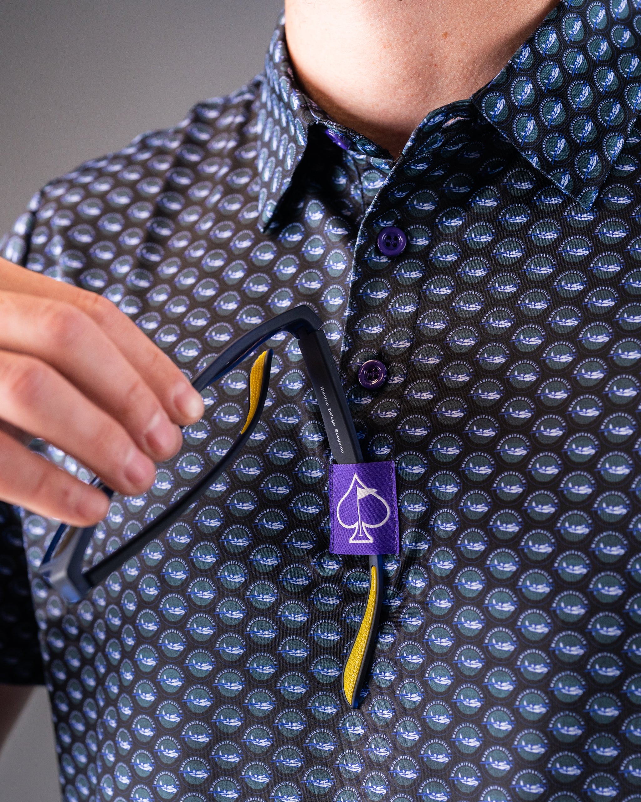 Bold golf shirt featuring a repeating pattern of blue, green, and purple logos, with purple buttons and a purple spade tag.