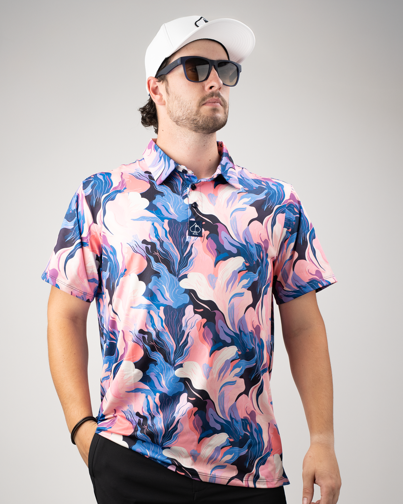 A golfer models a vibrant Melting Floral polo shirt featuring swirling pink, blue, and white floral patterns.