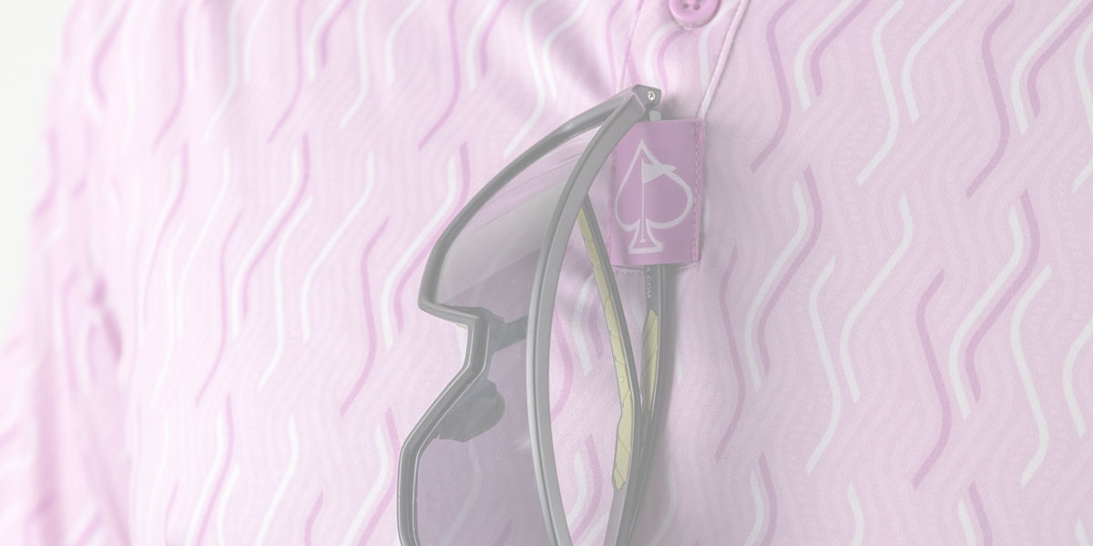 Pink golf apparel with a purple spade logo tag, featuring a clear glasses holder attached to the fabric.