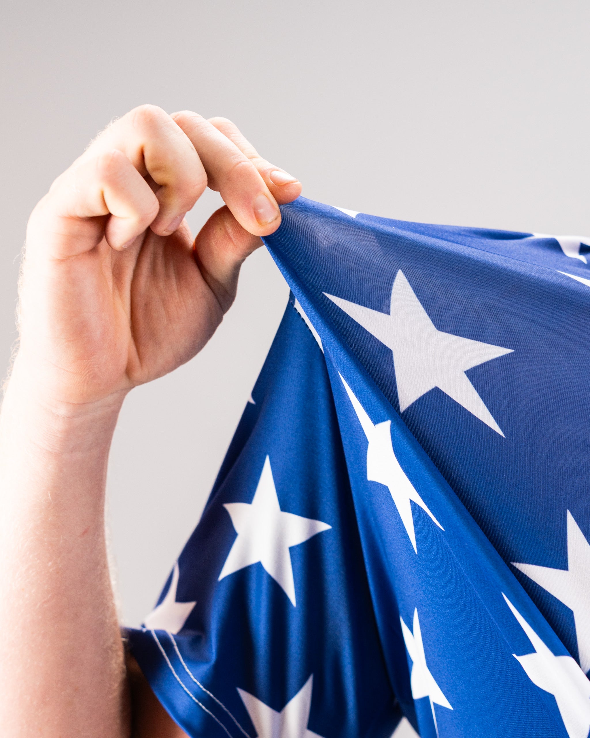 Close-up of a hand holding and slightly pulling a blue fabric with white stars, resembling a patriotic flag or banner.