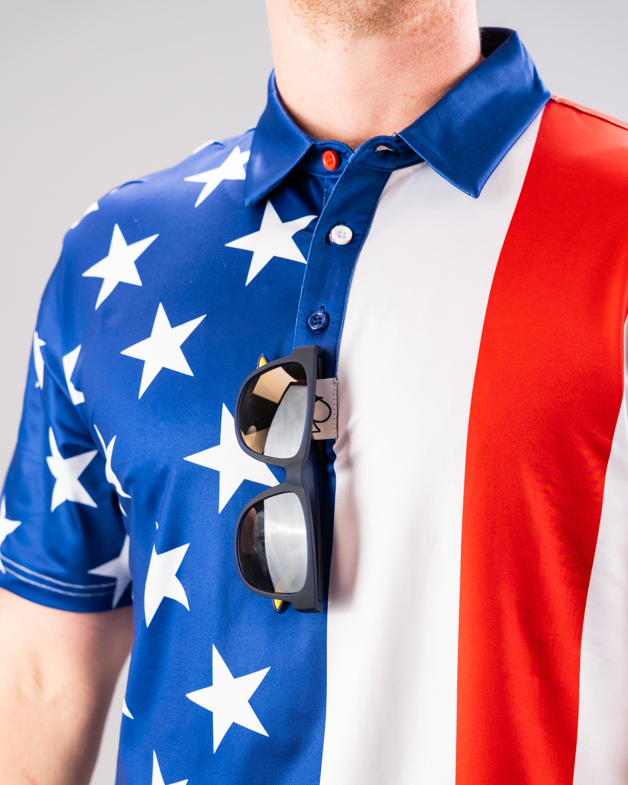 A person wearing a patriotic shirt with an American flag design, featuring blue with white stars and red and white stripes, with sunglasses hanging from the collar.