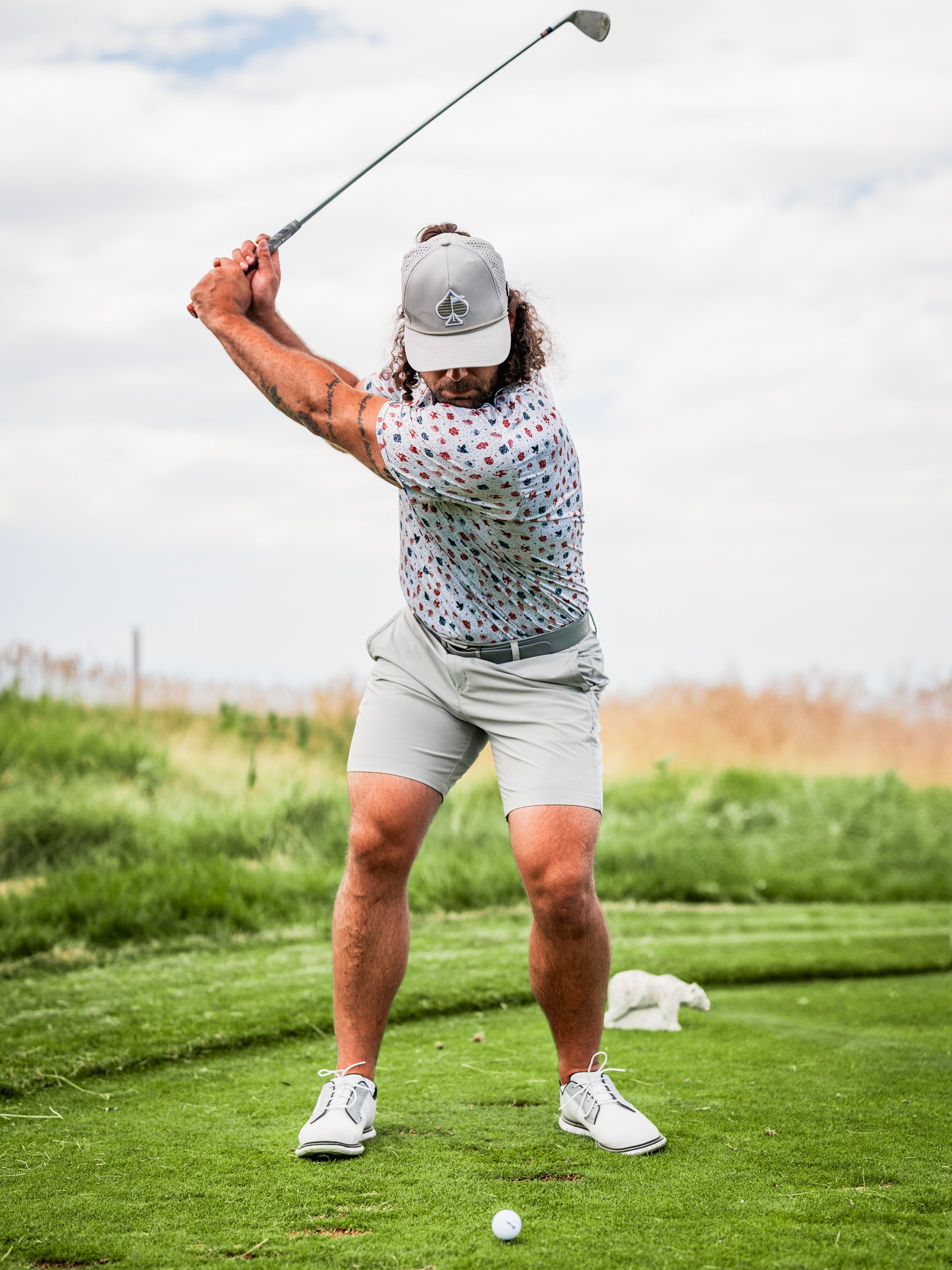A golfer in a colorful patterned shirt and gray shorts prepares to swing on a lush green course.