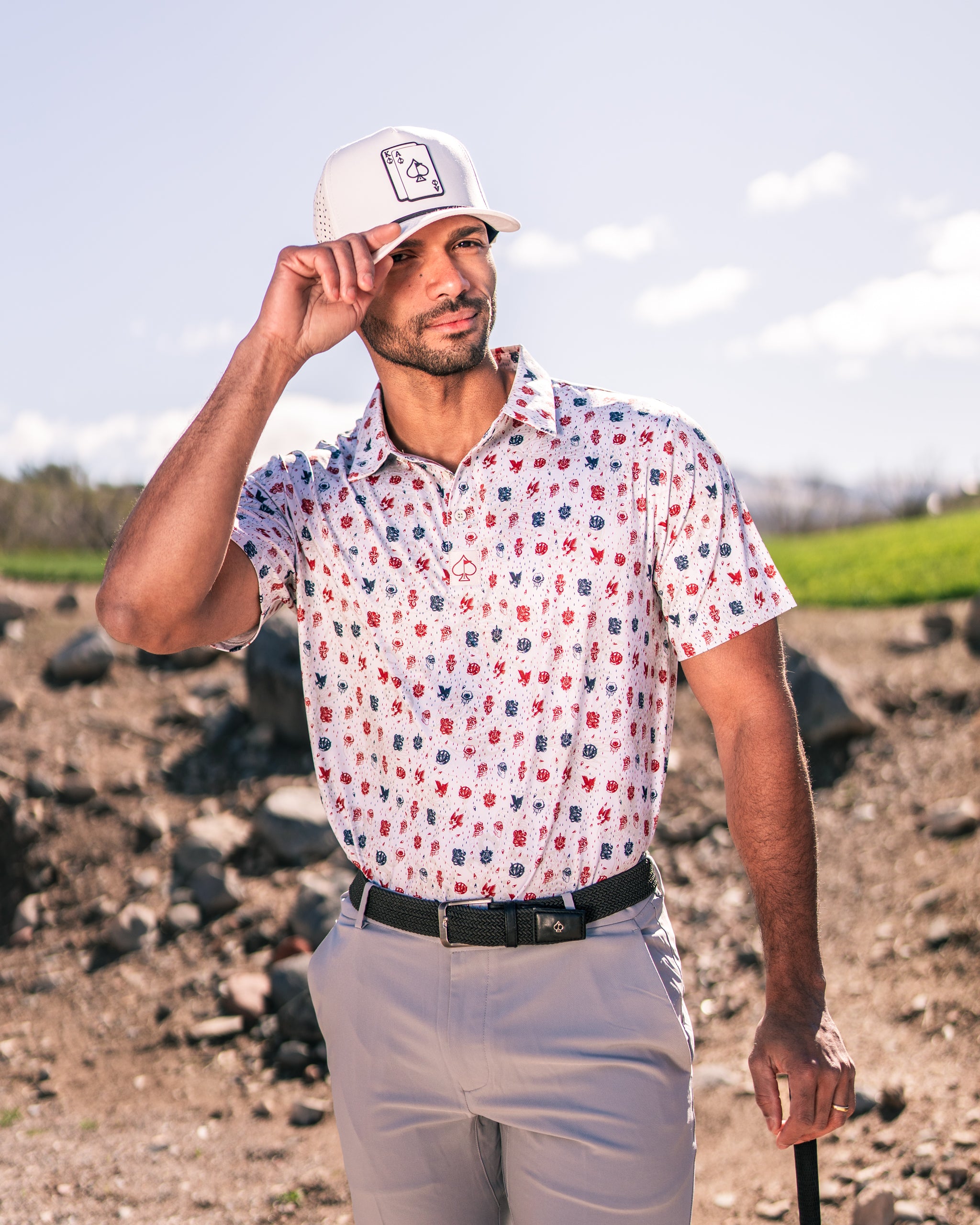 A golfer wearing an American Traditional polo shirt with a colorful pattern, adjusting his cap on a sunny course.