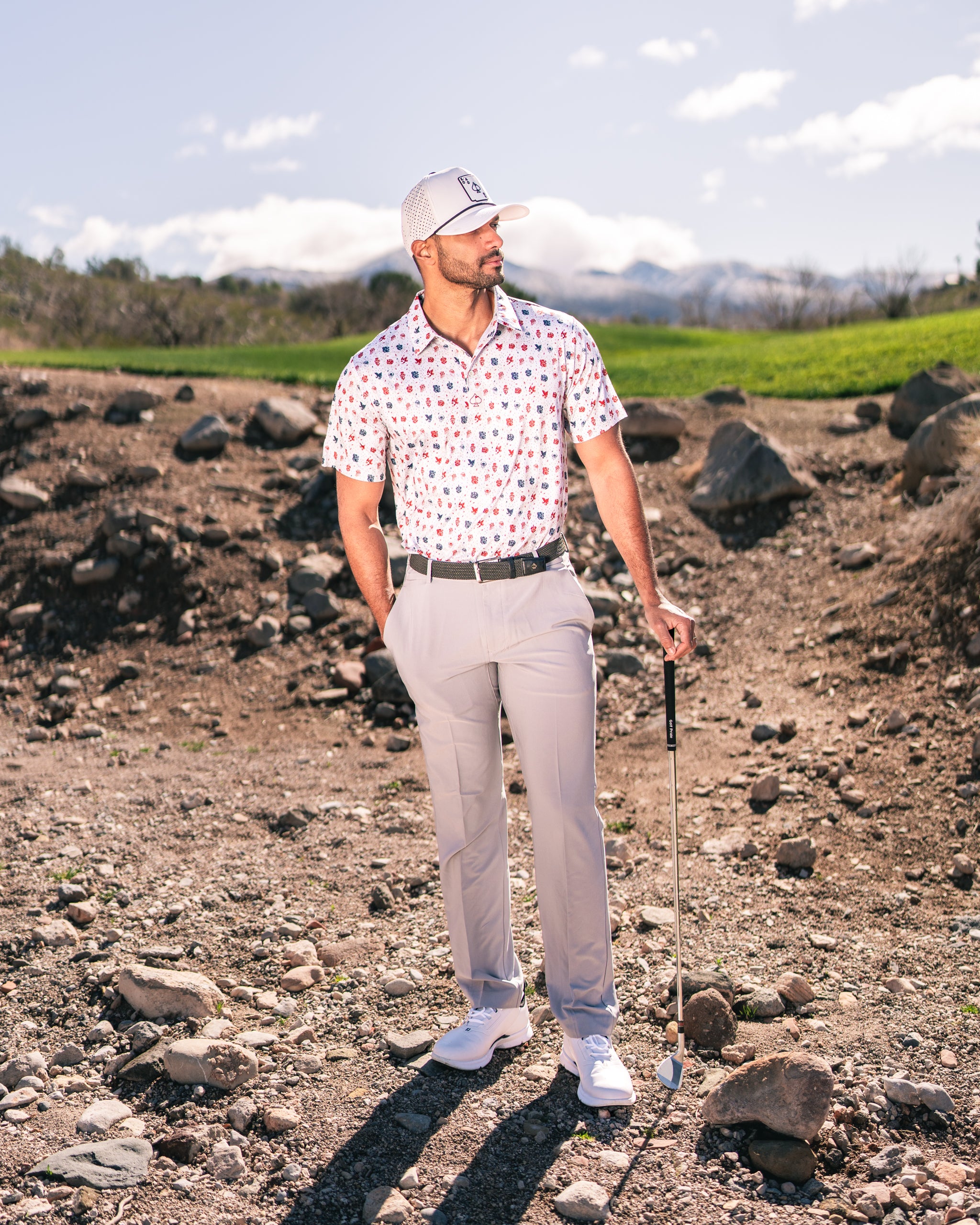 Man in a colorful American Traditional golf shirt stands confidently on a rocky course, holding a golf club.