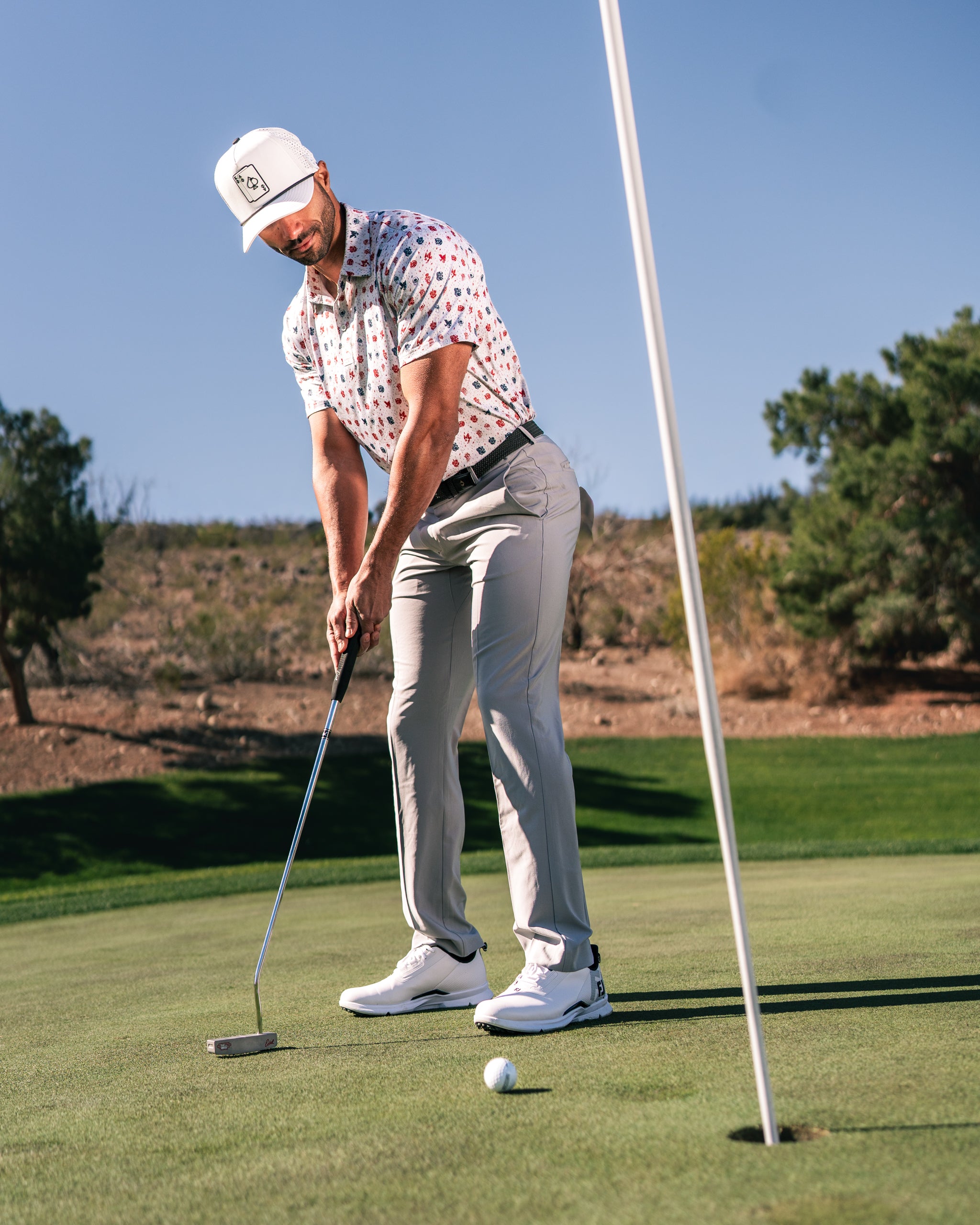 A golfer in a patterned shirt and cap putts on the green, showcasing bold golf apparel and a stylish look.