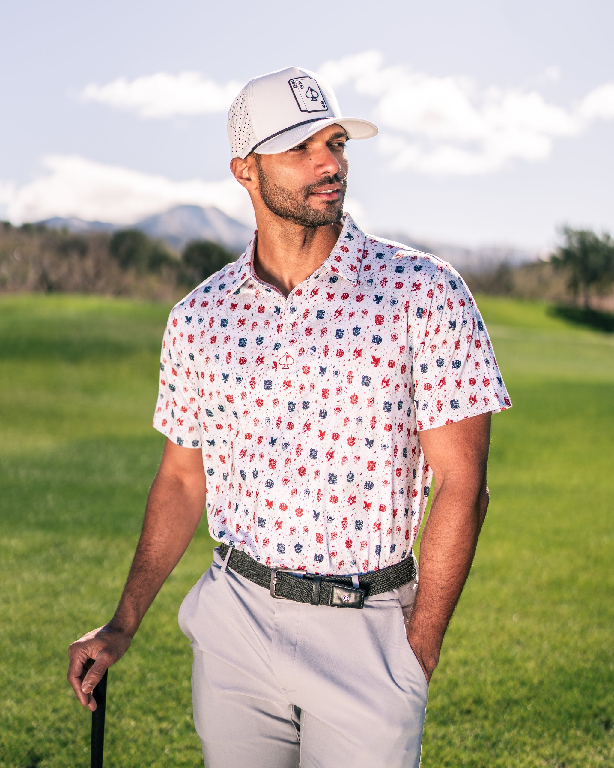 A golfer wearing an American Traditional polo shirt with a colorful pattern stands on a golf course, holding a club.