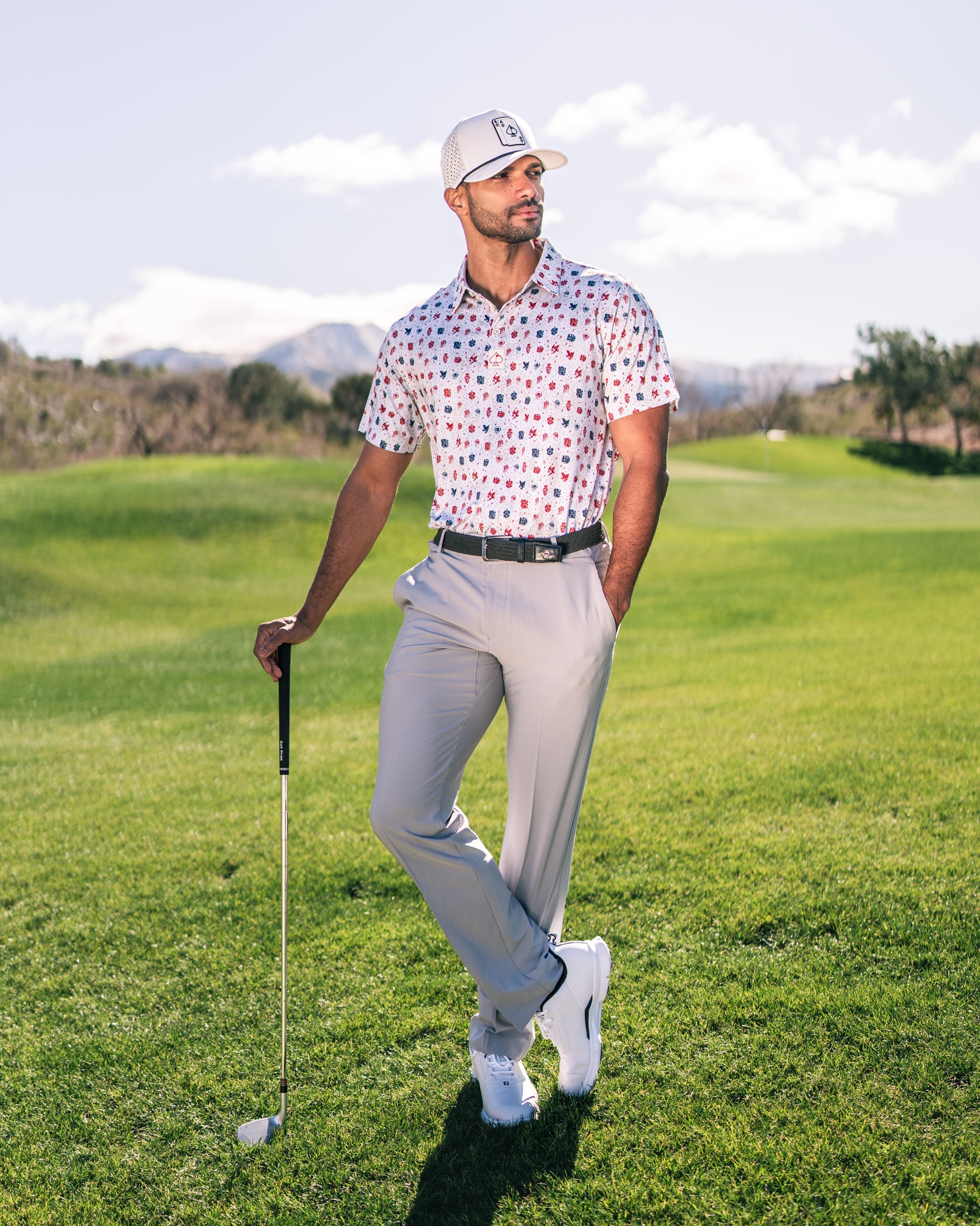 A golfer stands confidently on the course, wearing a colorful American Traditional polo shirt and light gray pants.