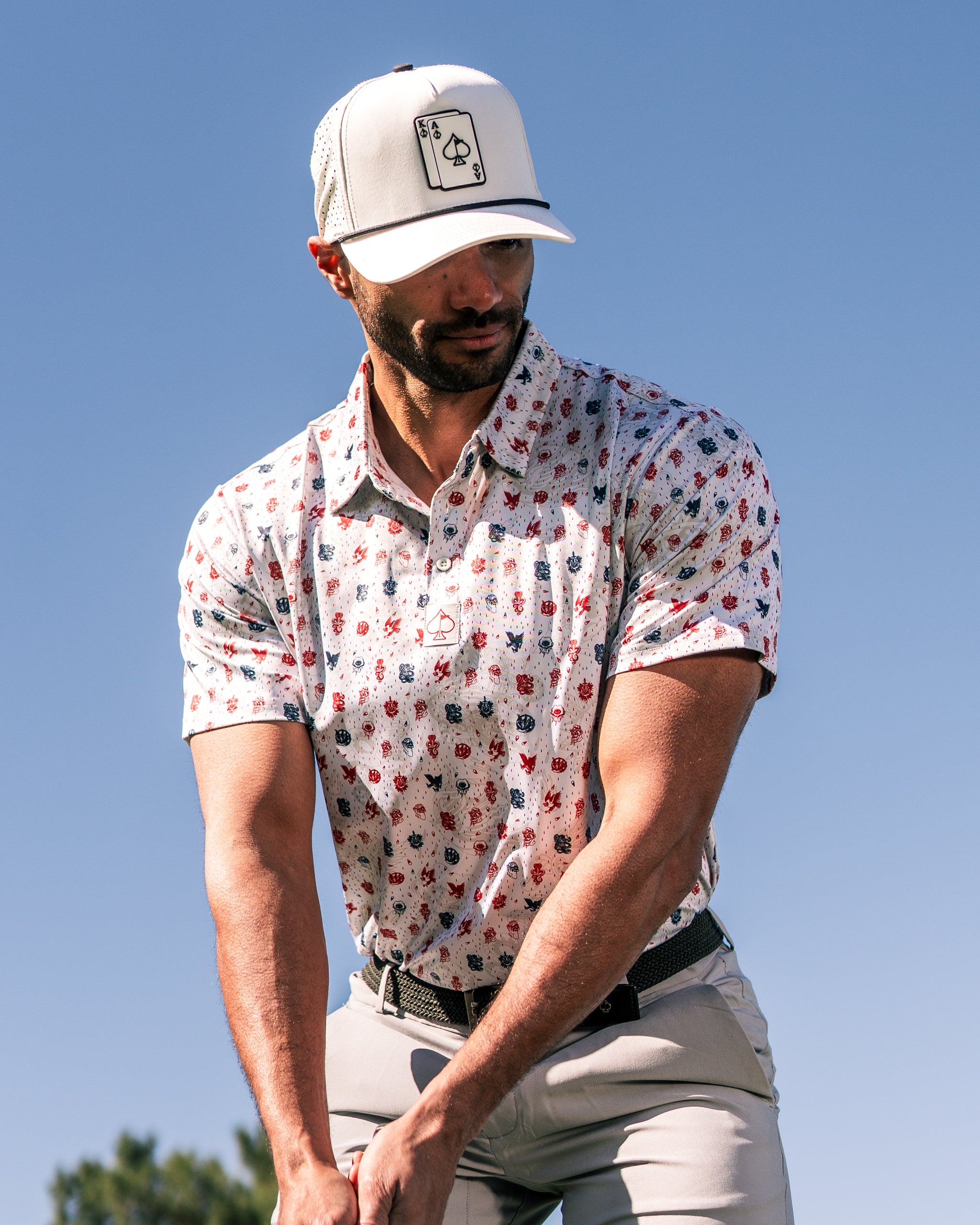 Stylish golfer wearing an American Traditional polo shirt and a cap, preparing to swing on a sunny day.