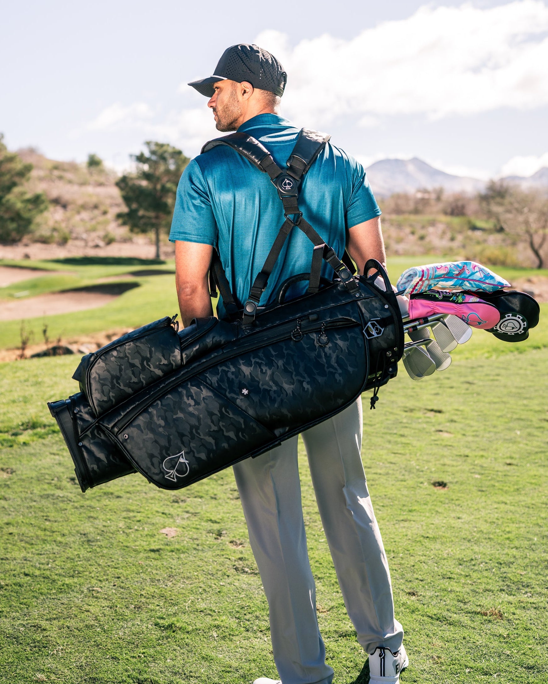 A golfer carries a stylish black camo golf bag over his shoulder on a sunny course, showcasing a modern, sporty look.