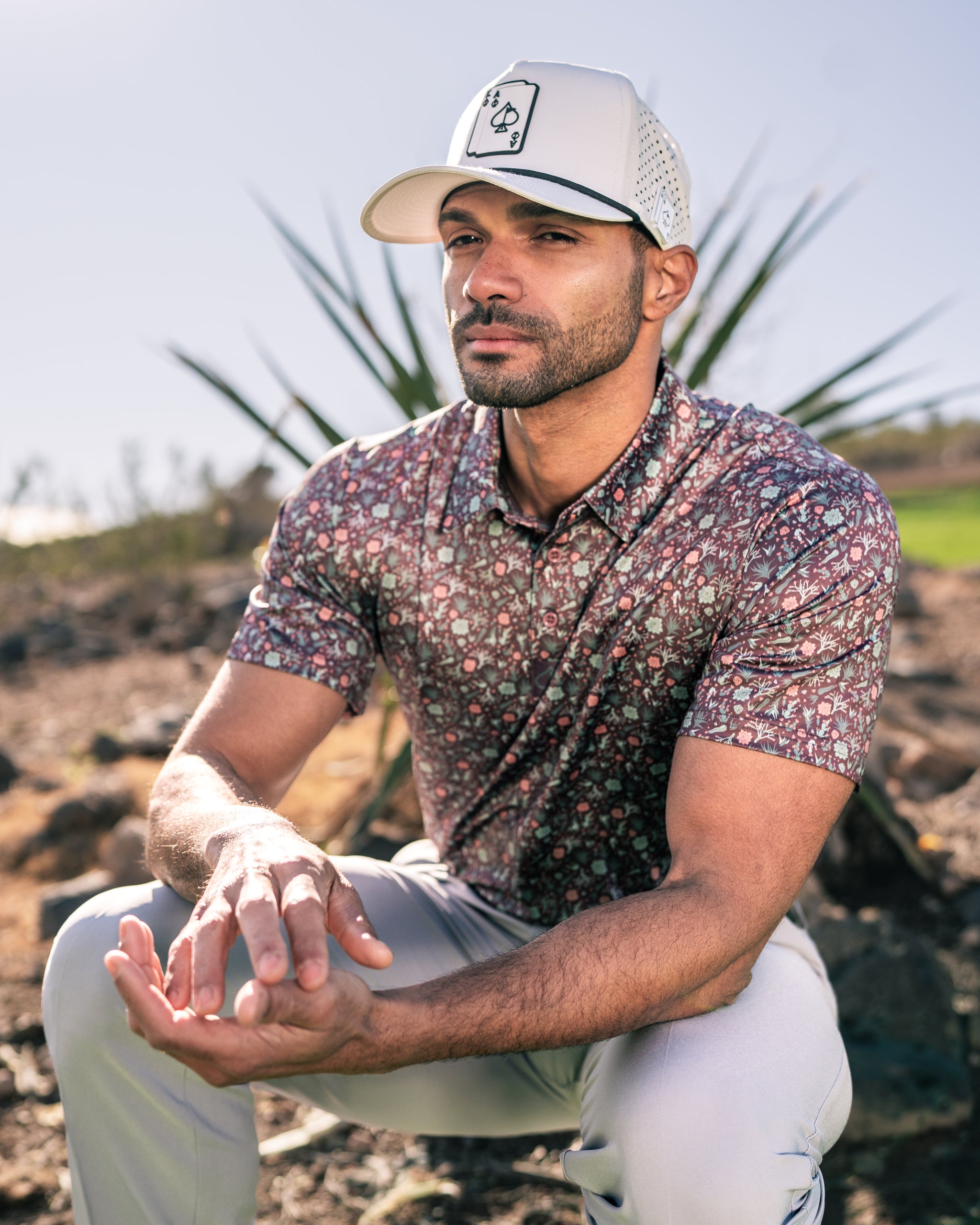 Man wearing a Desert Sage golf shirt with a floral pattern, seated outdoors against a desert landscape.