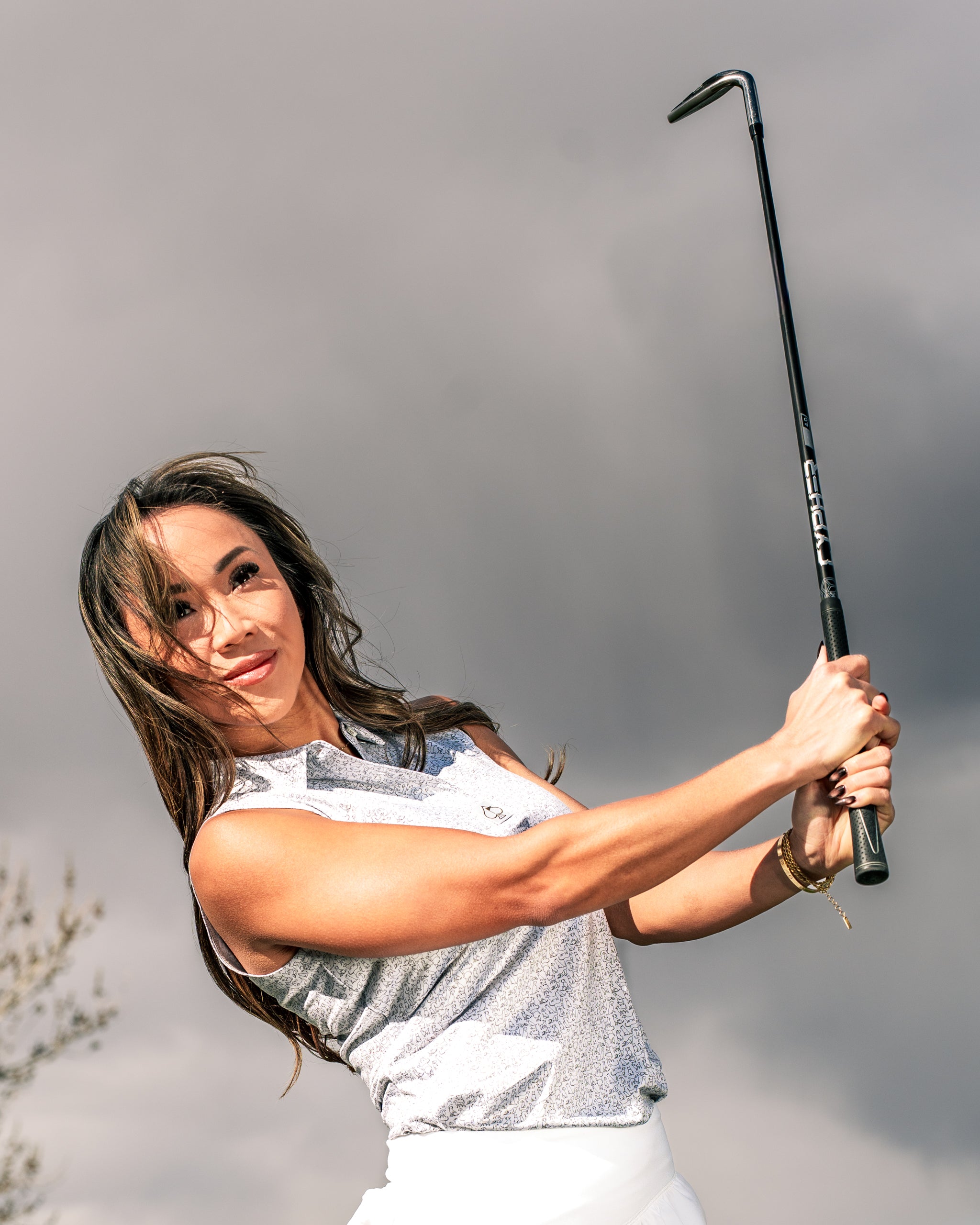 A woman swings a golf club, showcasing the Women's Best Friend Light golf apparel against a cloudy sky.