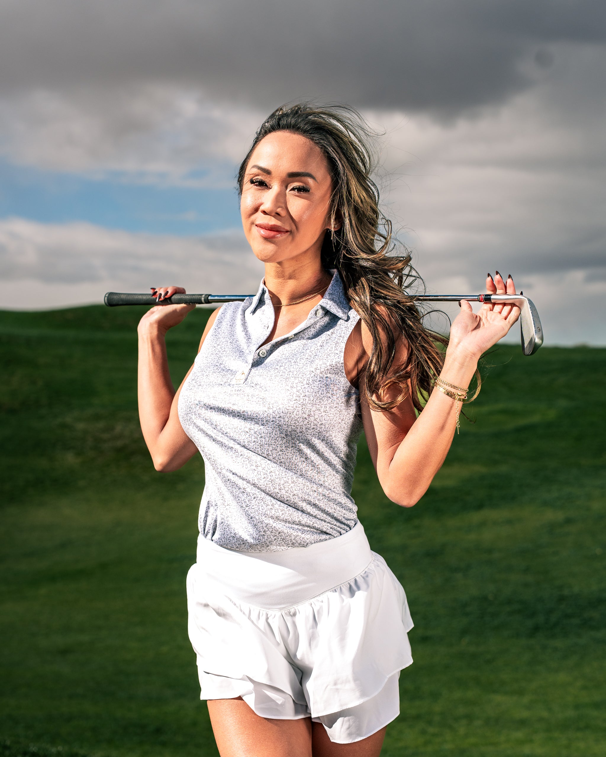 Confident woman in a stylish golf polo and white shorts, holding a golf club, posing on a lush green course.