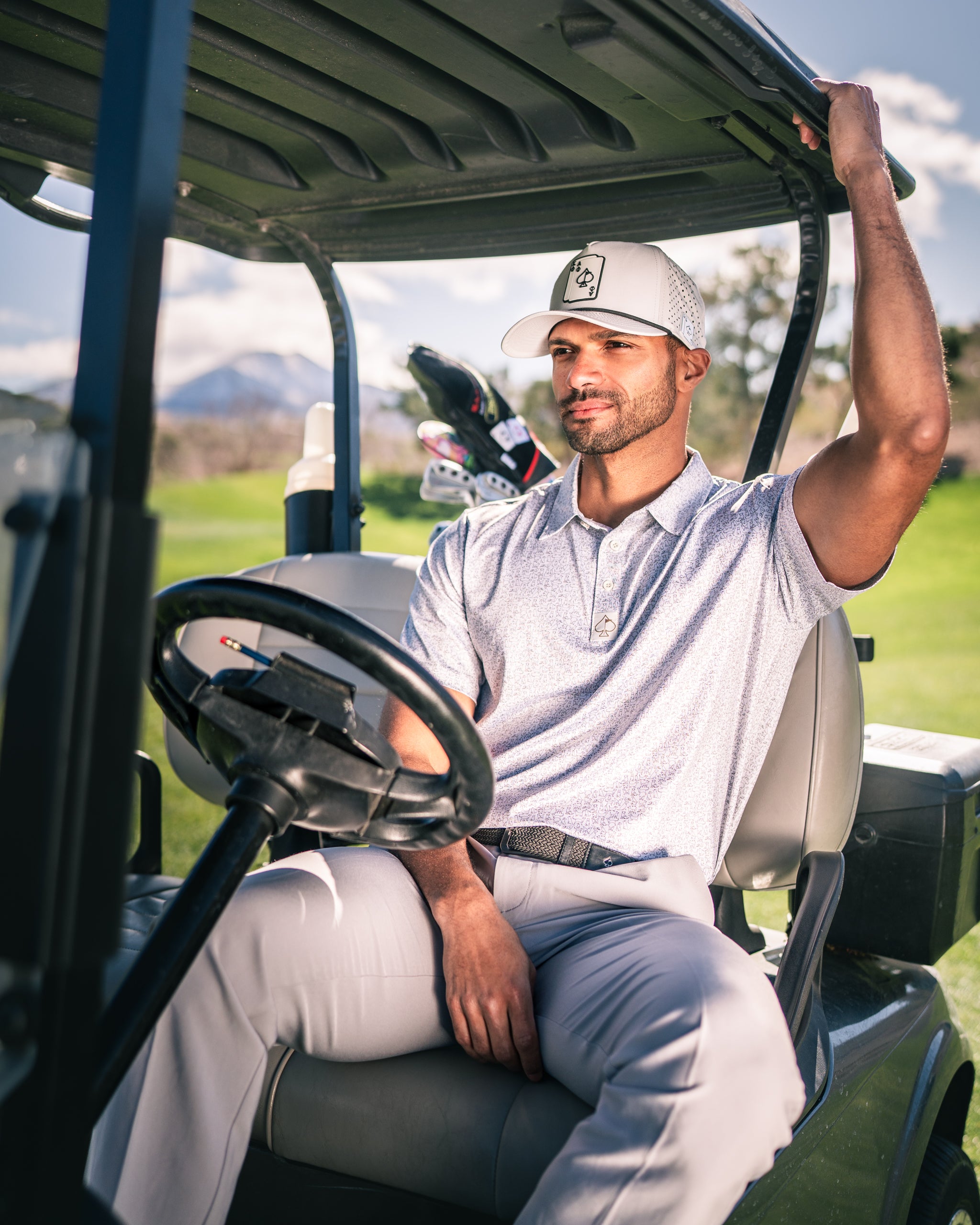 A golfer relaxes in a cart wearing a stylish polo and cap, showcasing a confident look on the course.
