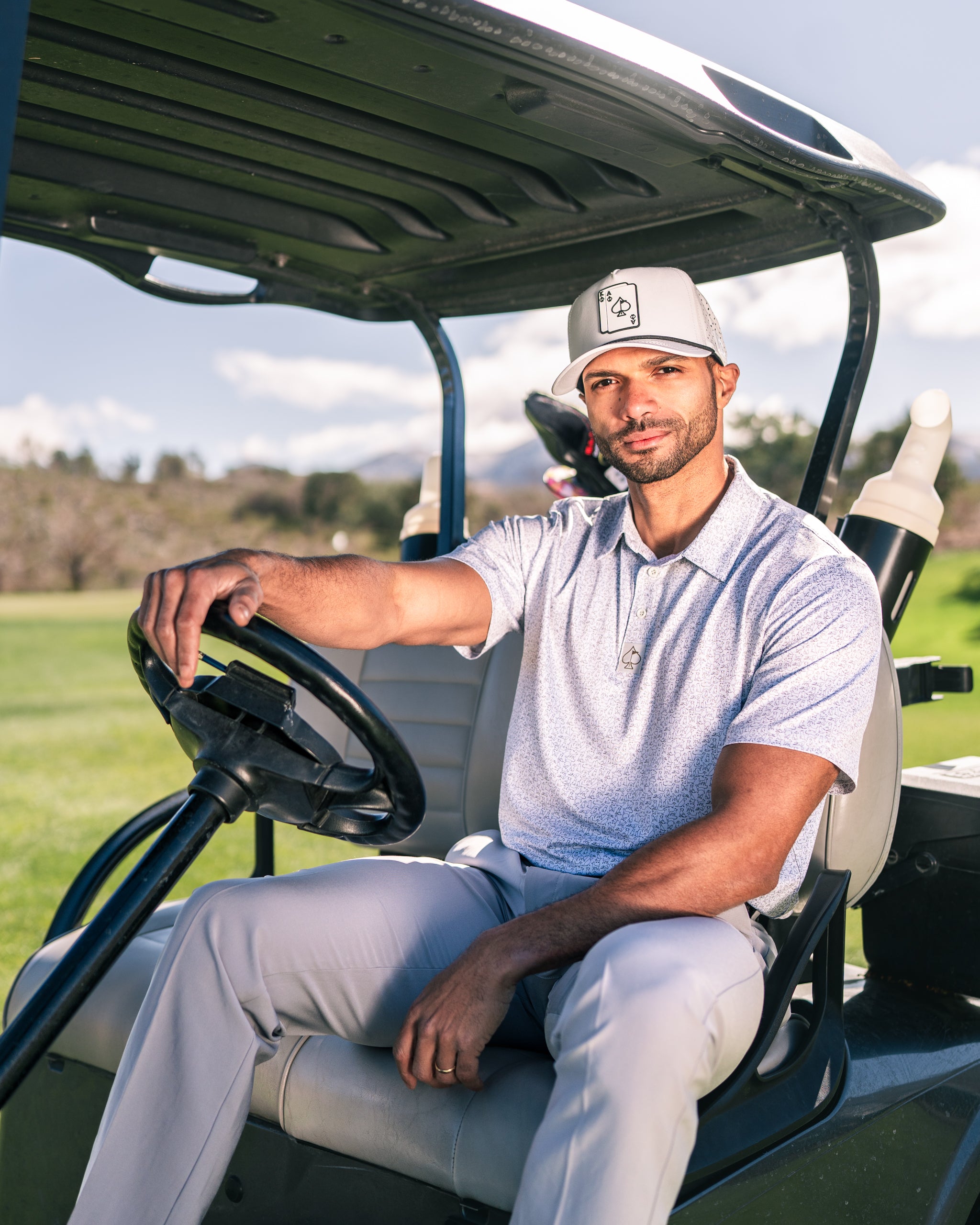 Man sitting in a golf cart wearing a stylish golf polo and cap, ready for a day on the course.