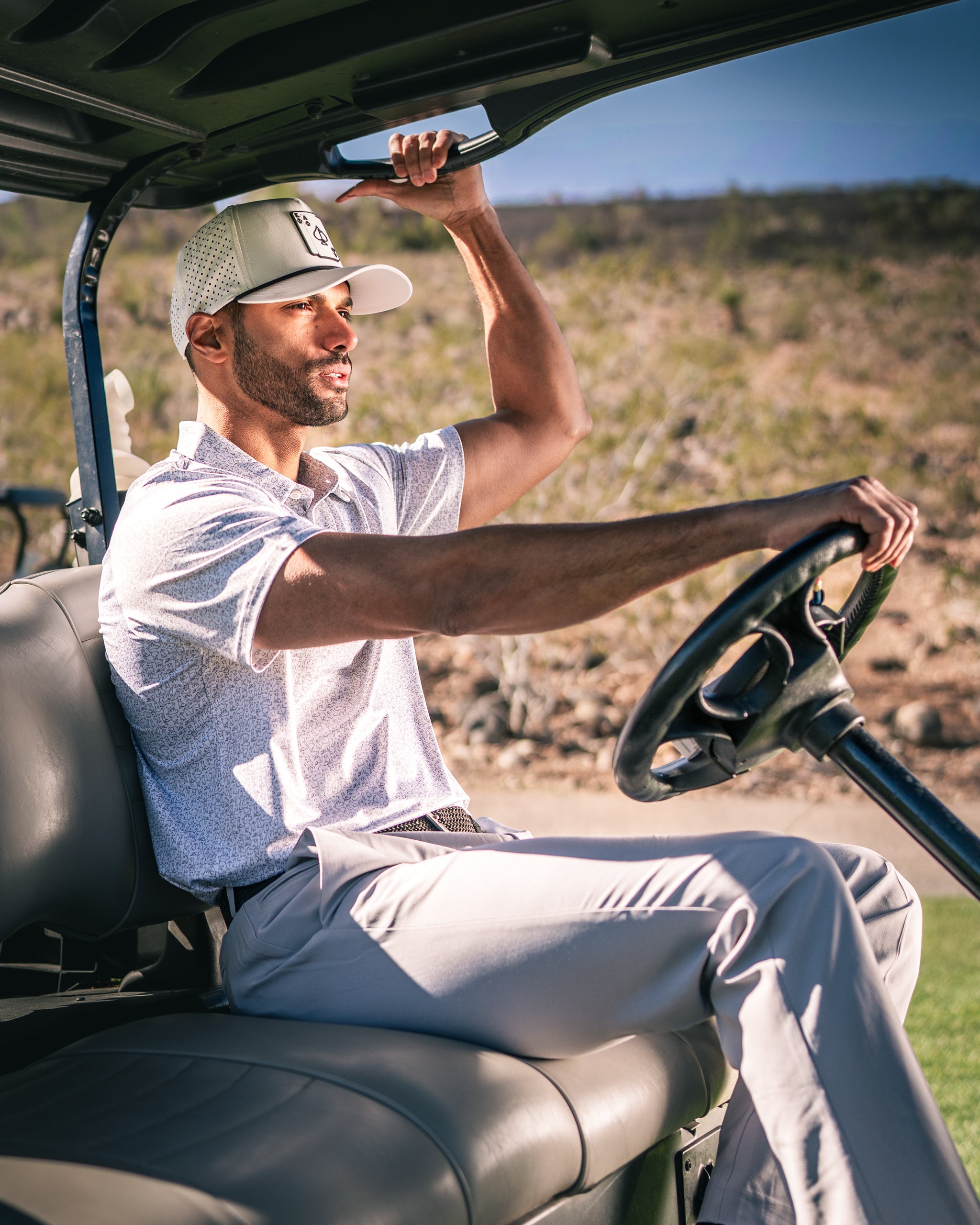 A golfer wearing a light shirt and cap sits in a golf cart, enjoying a sunny day on the course.