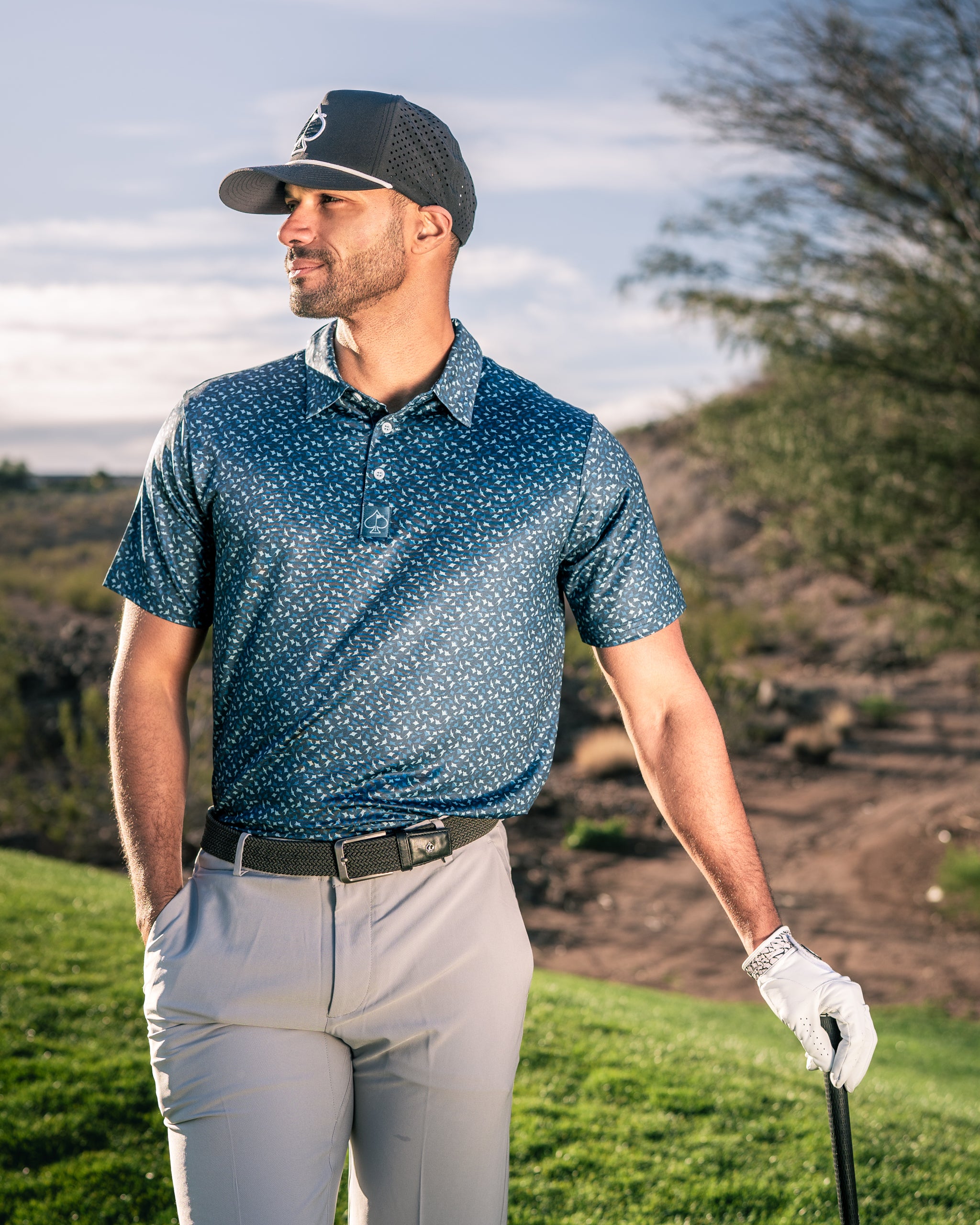 Man wearing a stylish blue Manta Ray golf polo with a subtle pattern, standing confidently on a golf course.