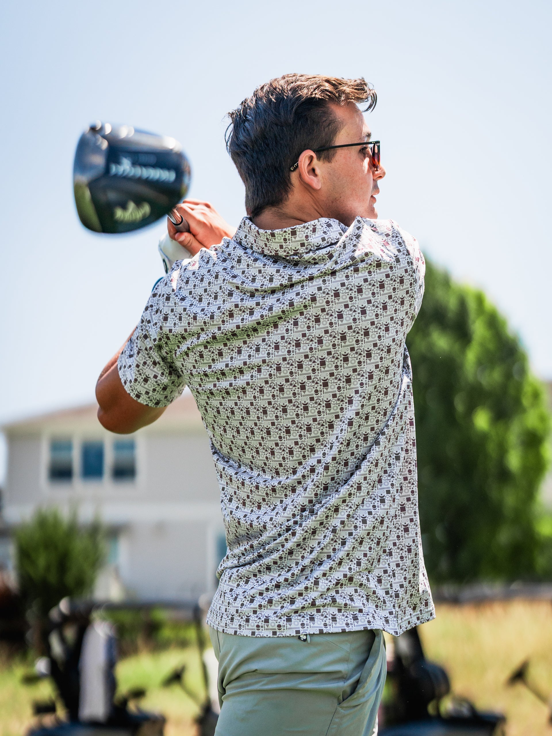 A golfer swings a club while wearing a stylish retro-patterned shirt, showcasing bold golf fashion on the course.